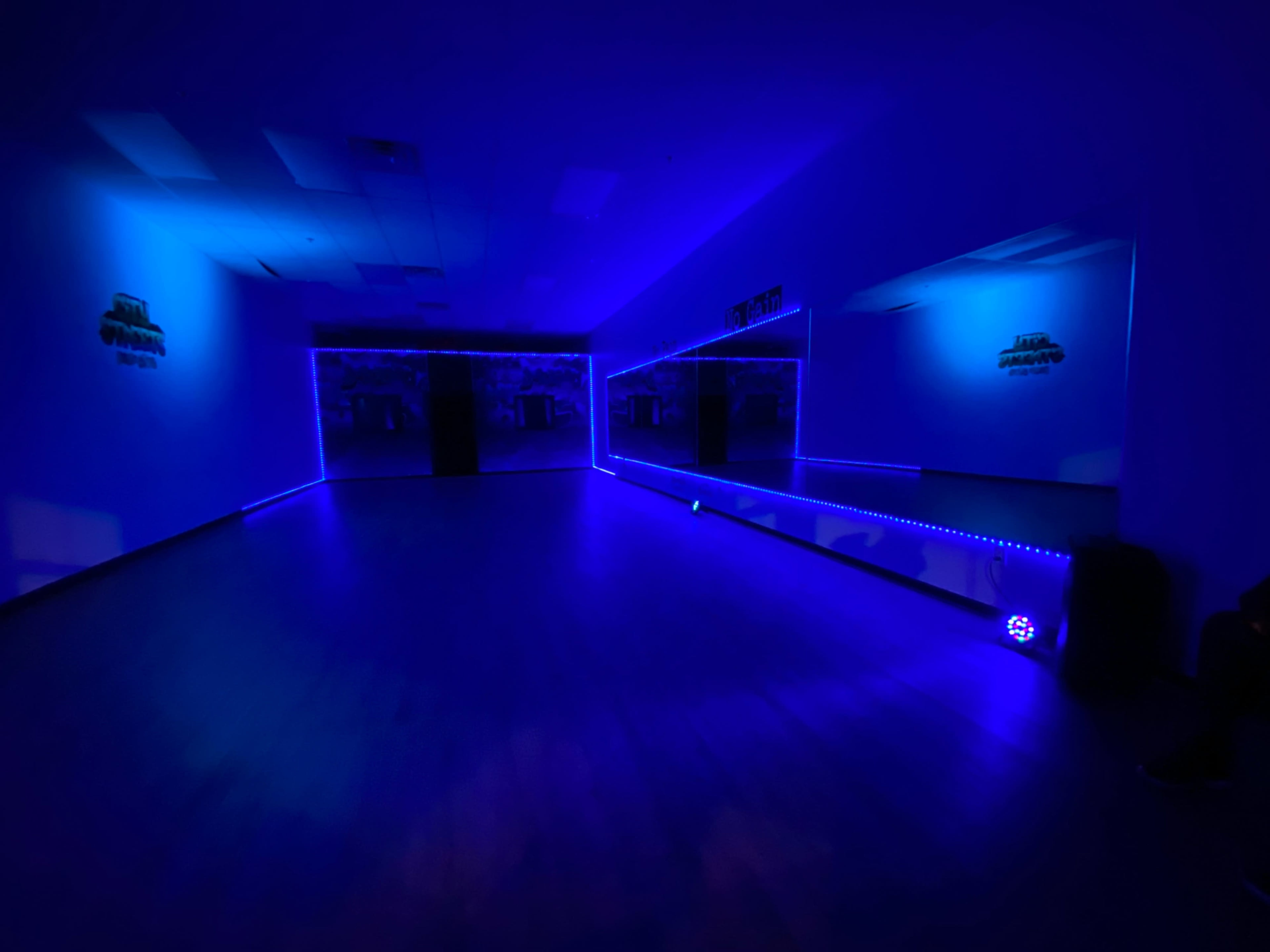 A dimly lit dance studio with blue LED lights illuminating the walls and mirrors.
