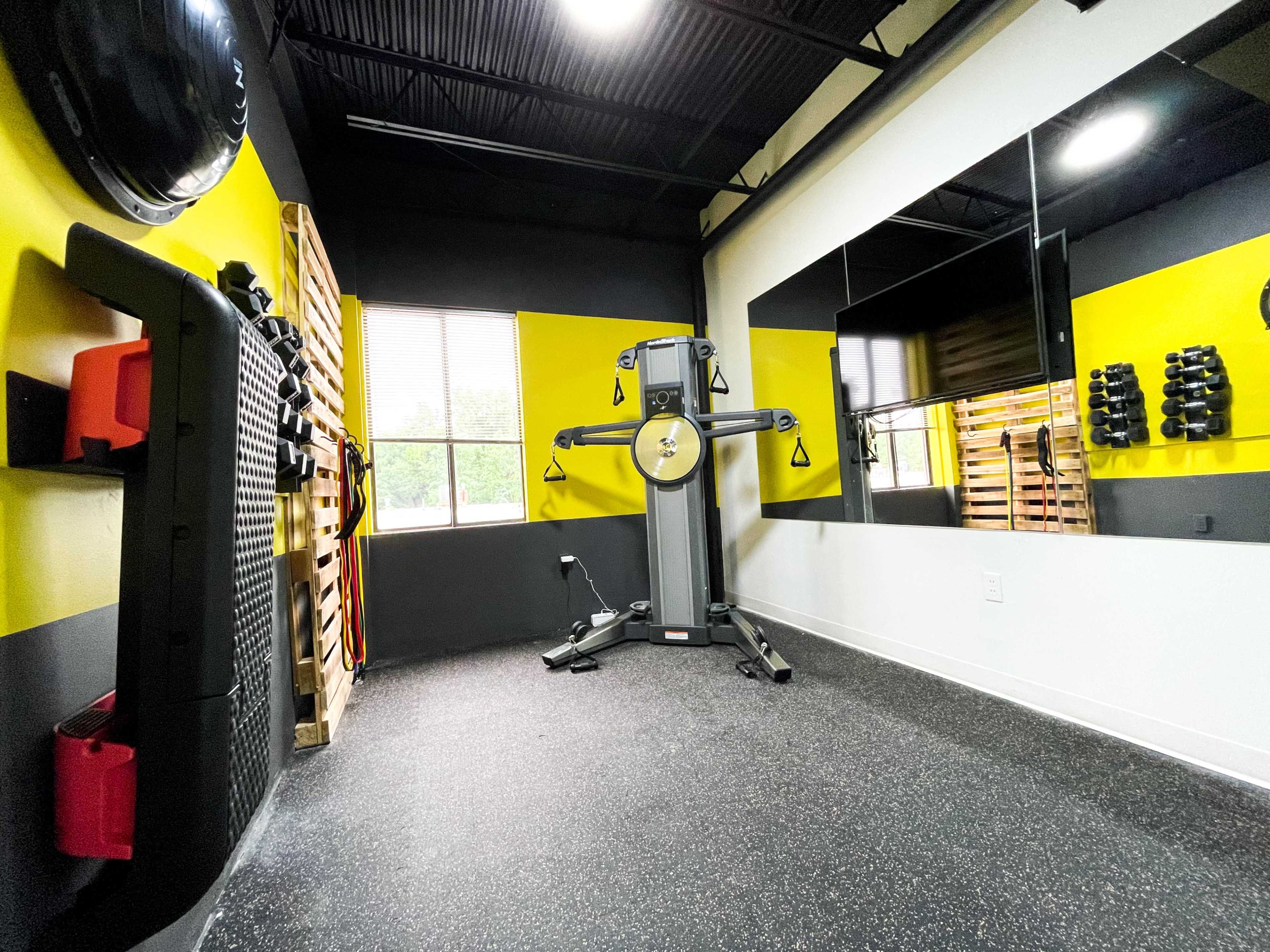 A gym interior with exercise equipment, including a multi-station gym machine, freestanding weights, and a fitness wall, all against a backdrop of black and yellow walls.