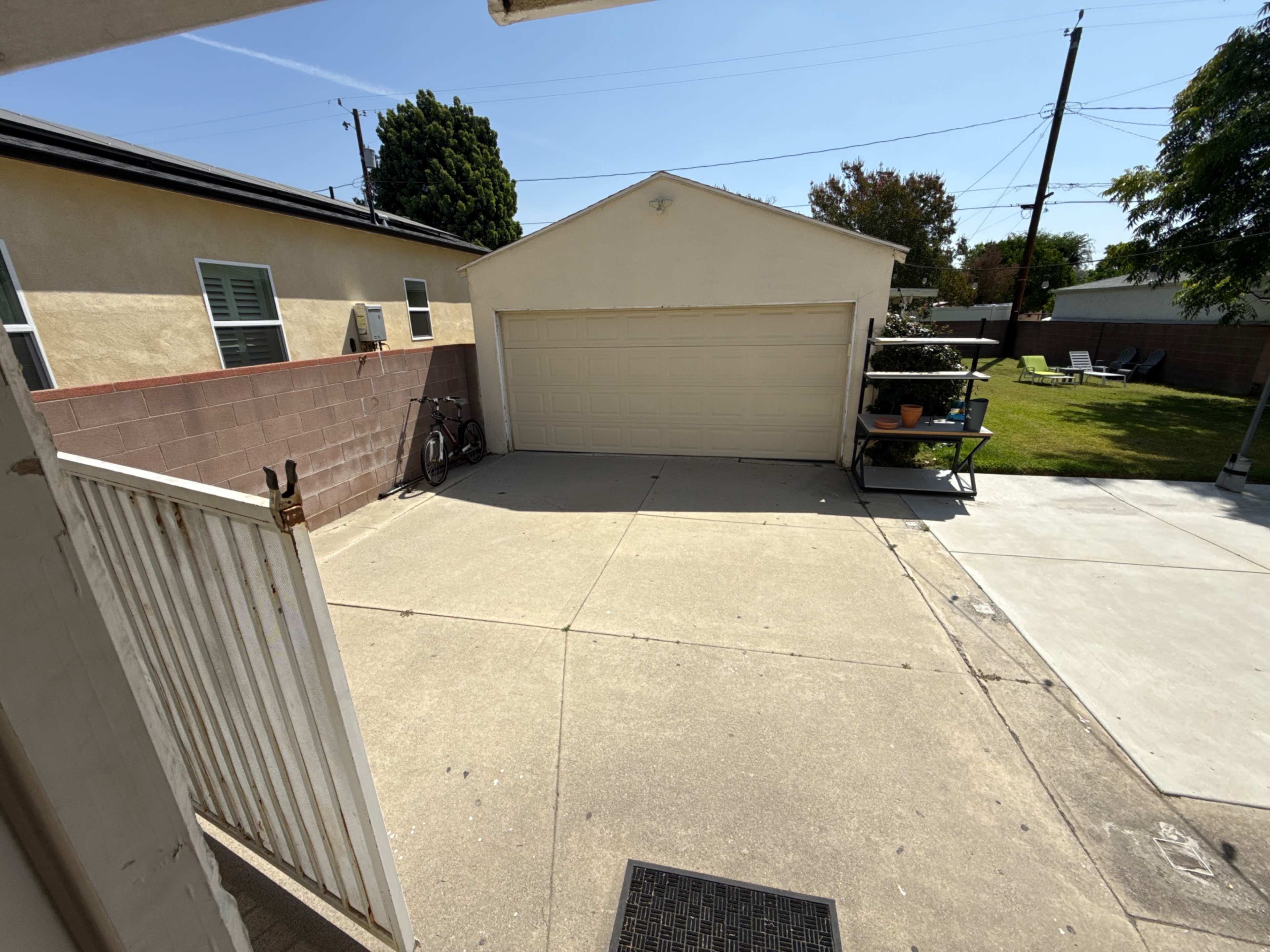A concrete driveway leads to a closed garage door, surrounded by a fenced yard and residential buildings.