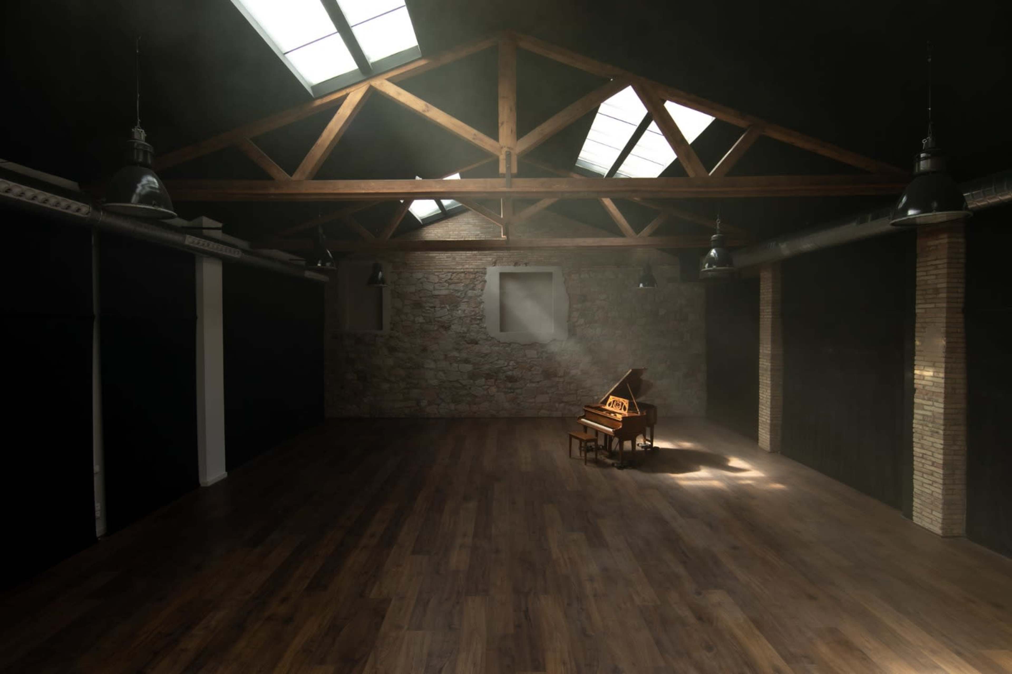 A grand piano sits in an empty room with wooden beams and large skylights illuminating the space.