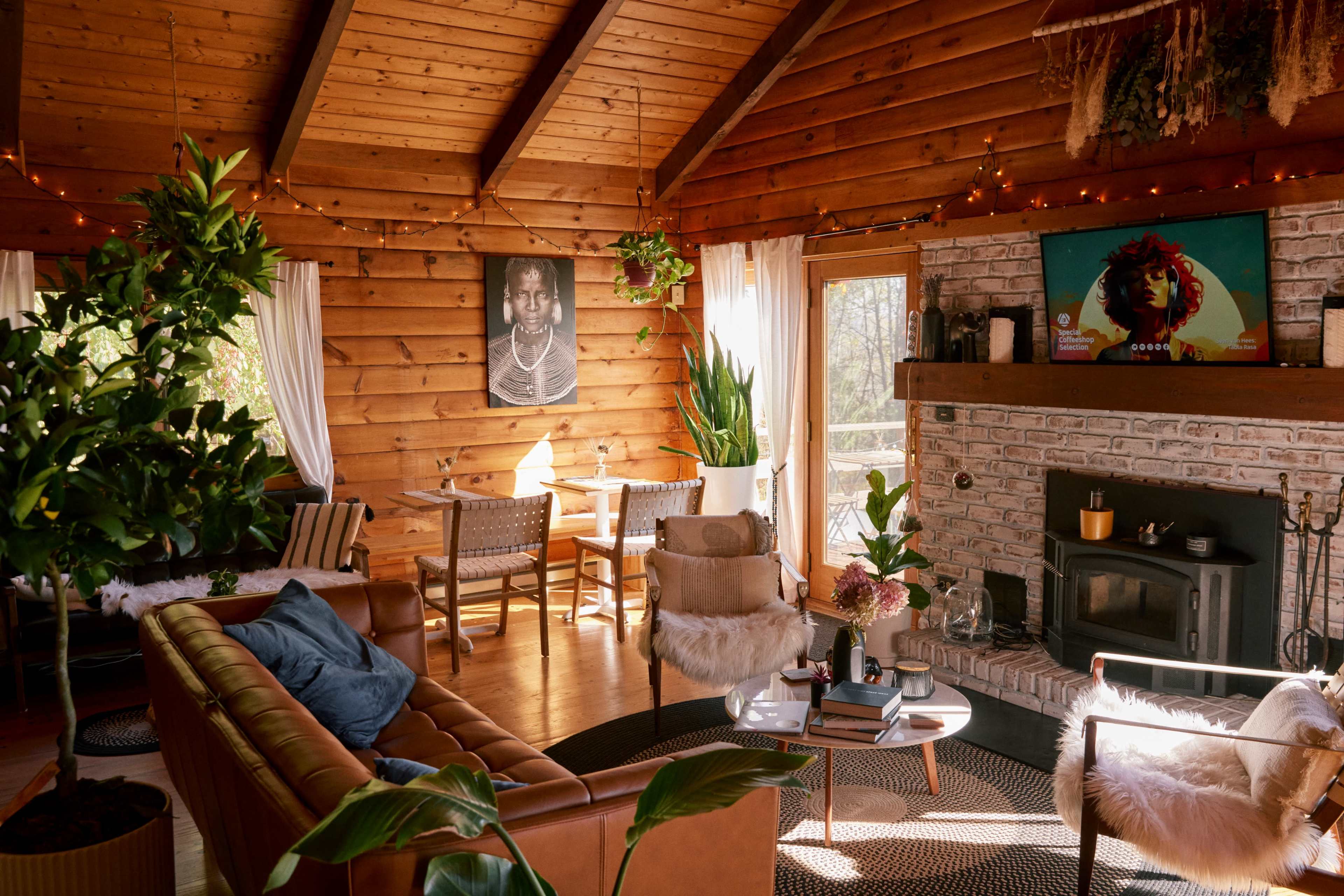 A cozy living room with wooden beams, a large leather sofa, potted plants, a fireplace, and artwork on the walls.