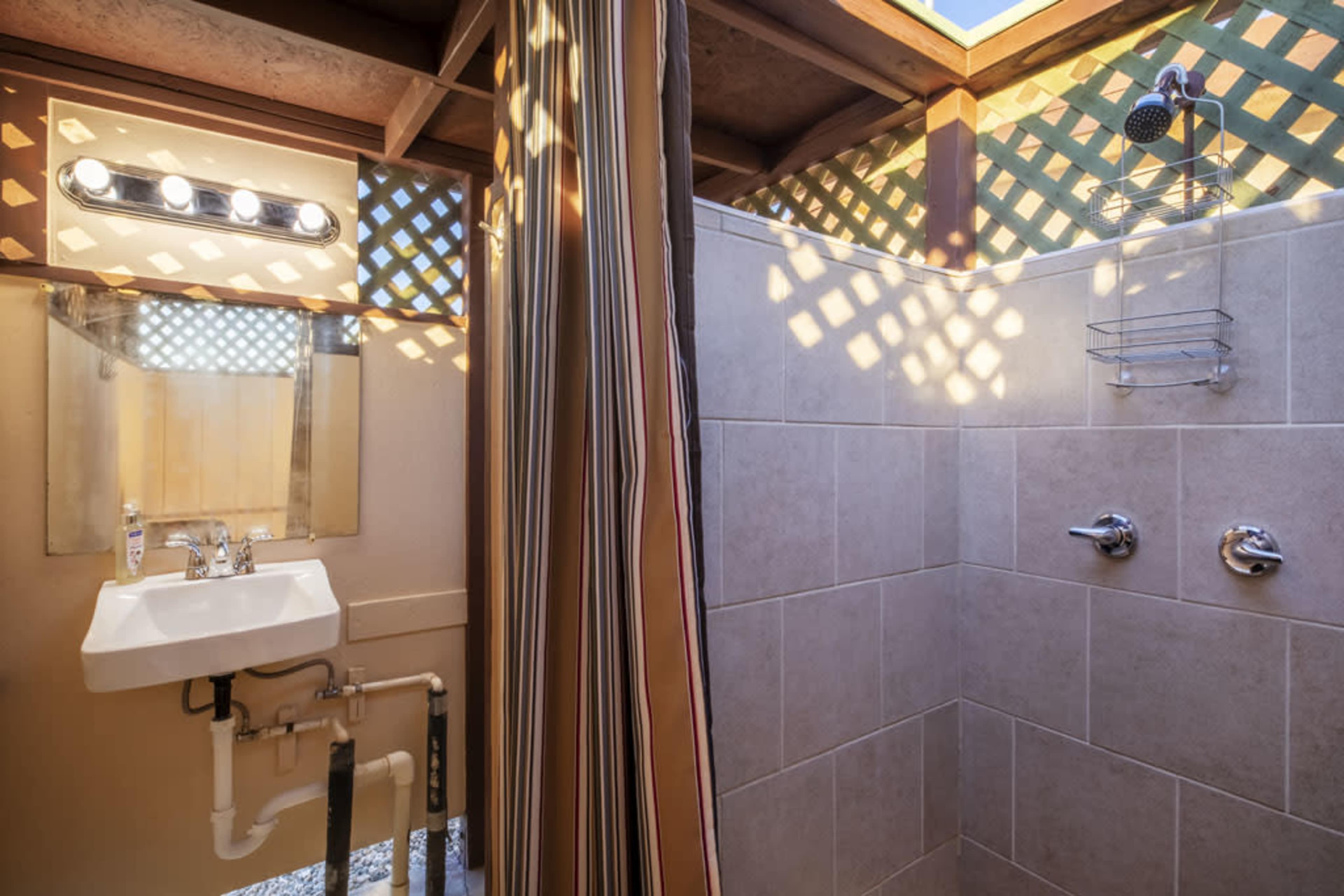 A shower area with a sink, both enclosed by a wooden framework and illuminated by natural light coming through a skylight.