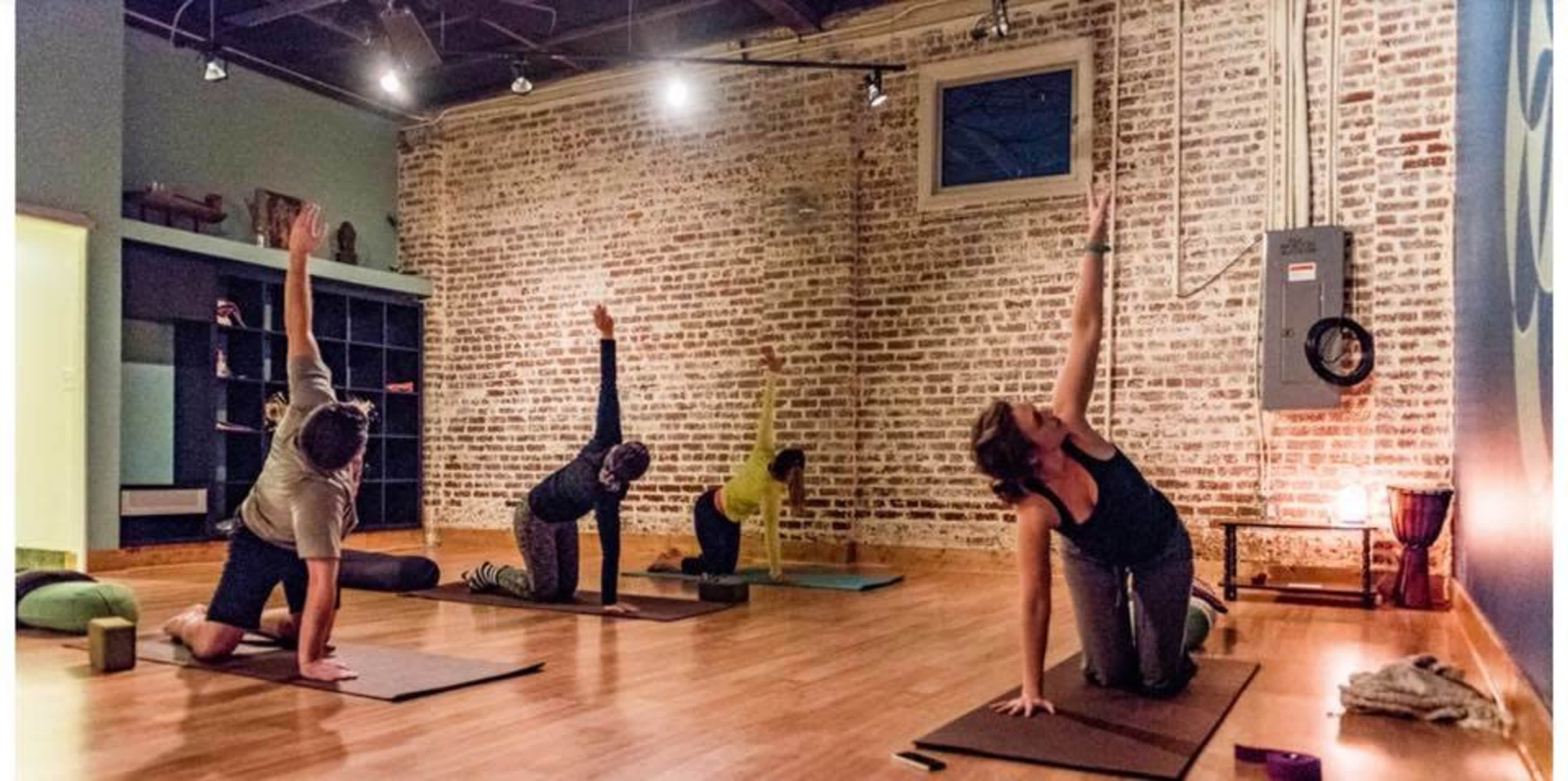 A group of six people is practicing yoga on mats in a studio with exposed brick walls.