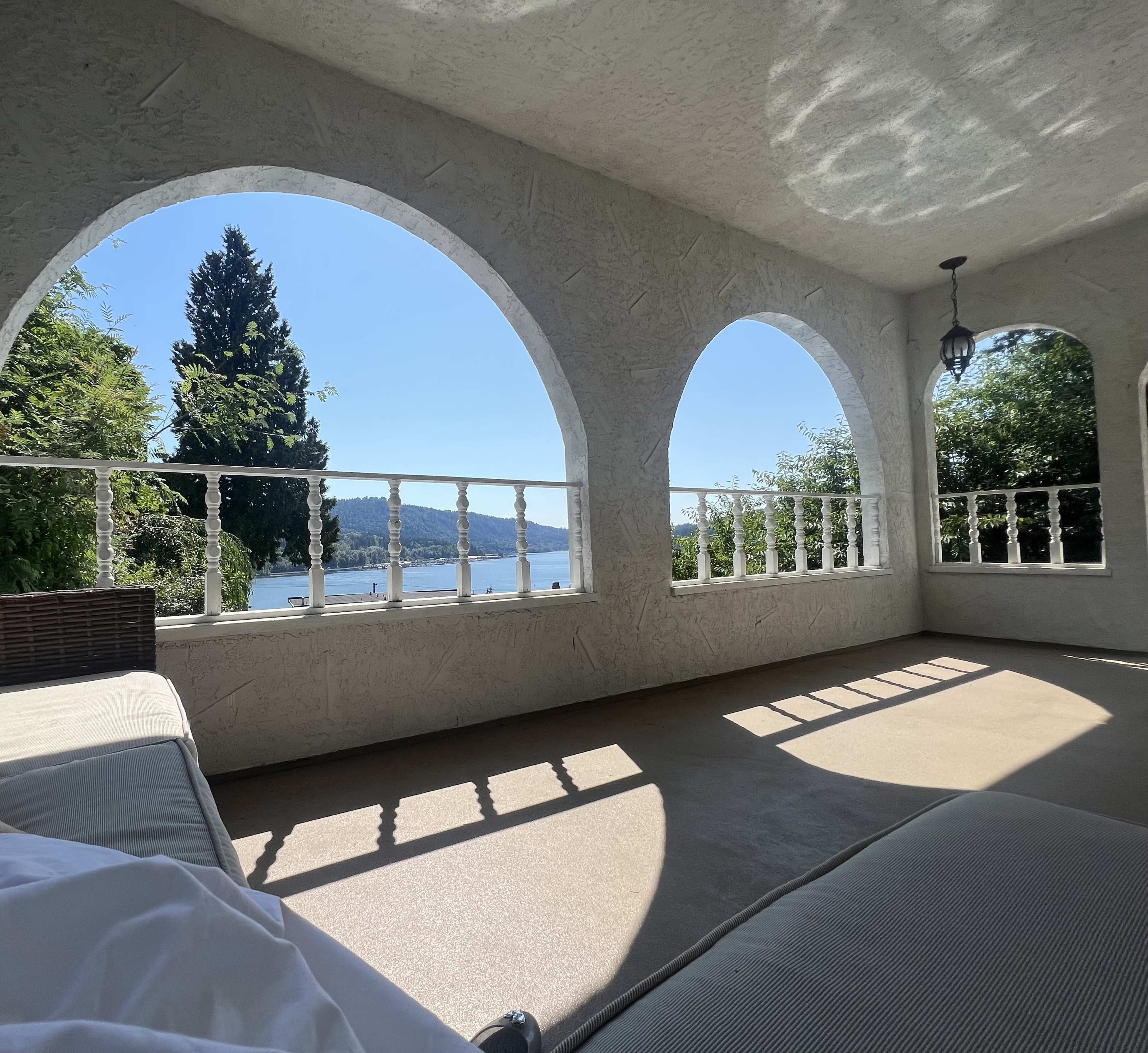 A spacious terrace with arched openings overlooking a lake and surrounding greenery.