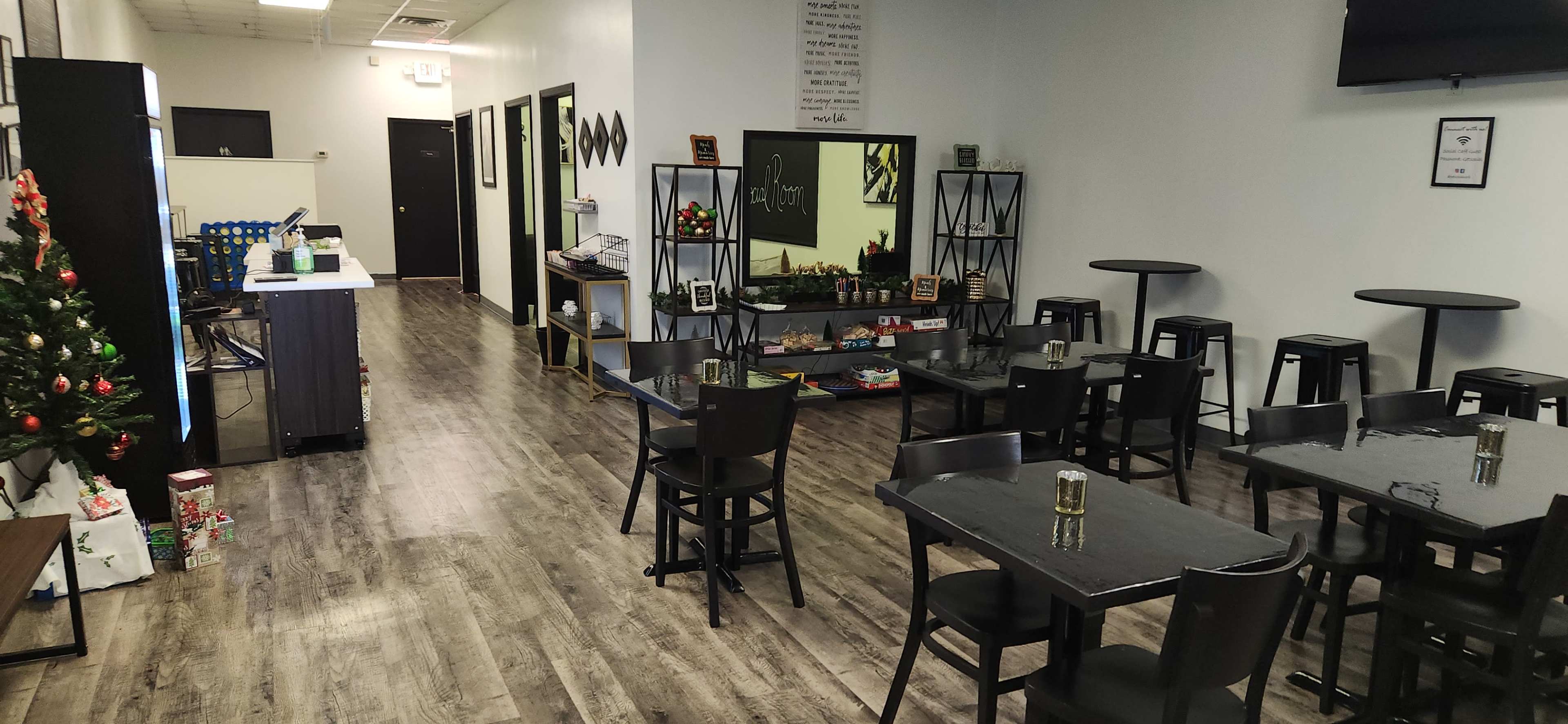 The image shows a modern, sparsely decorated dining area with black tables and chairs, a Christmas tree in one corner, and a counter backlit by a wall-mounted television.