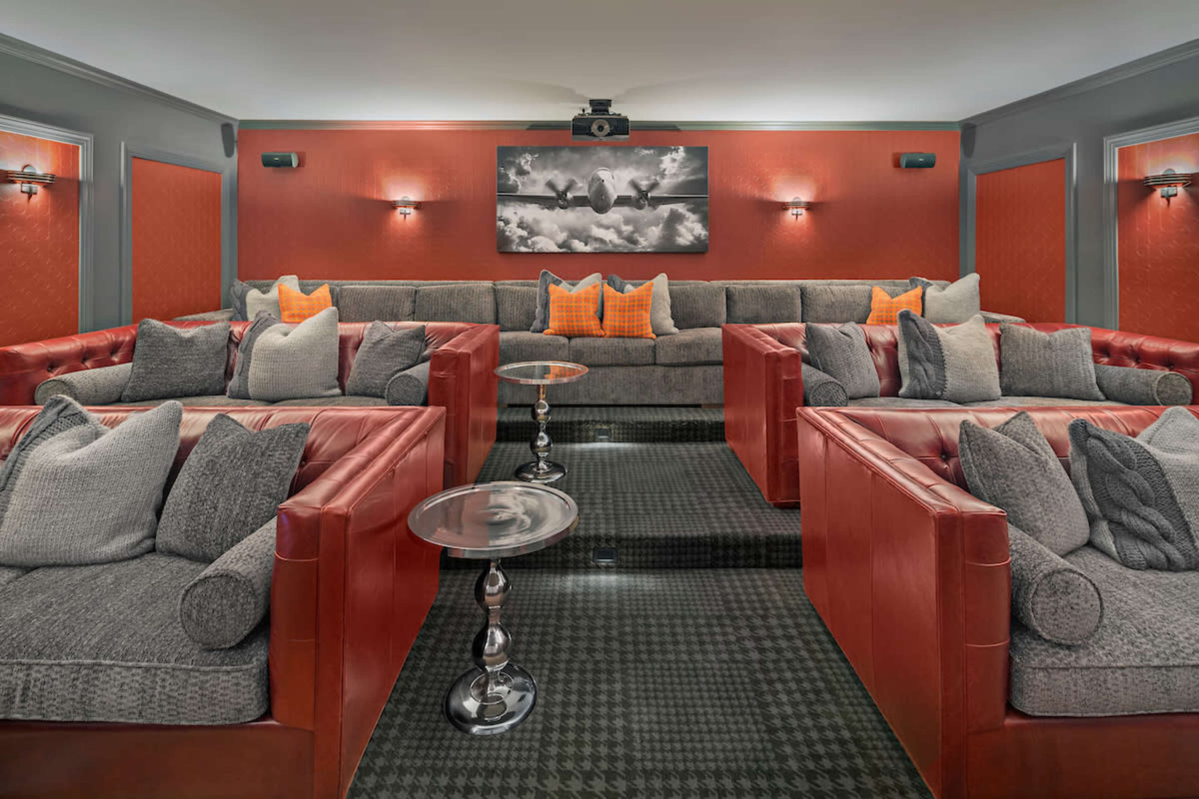 A home theater with multiple plush seating areas, featuring red leather couches and a large central screen.