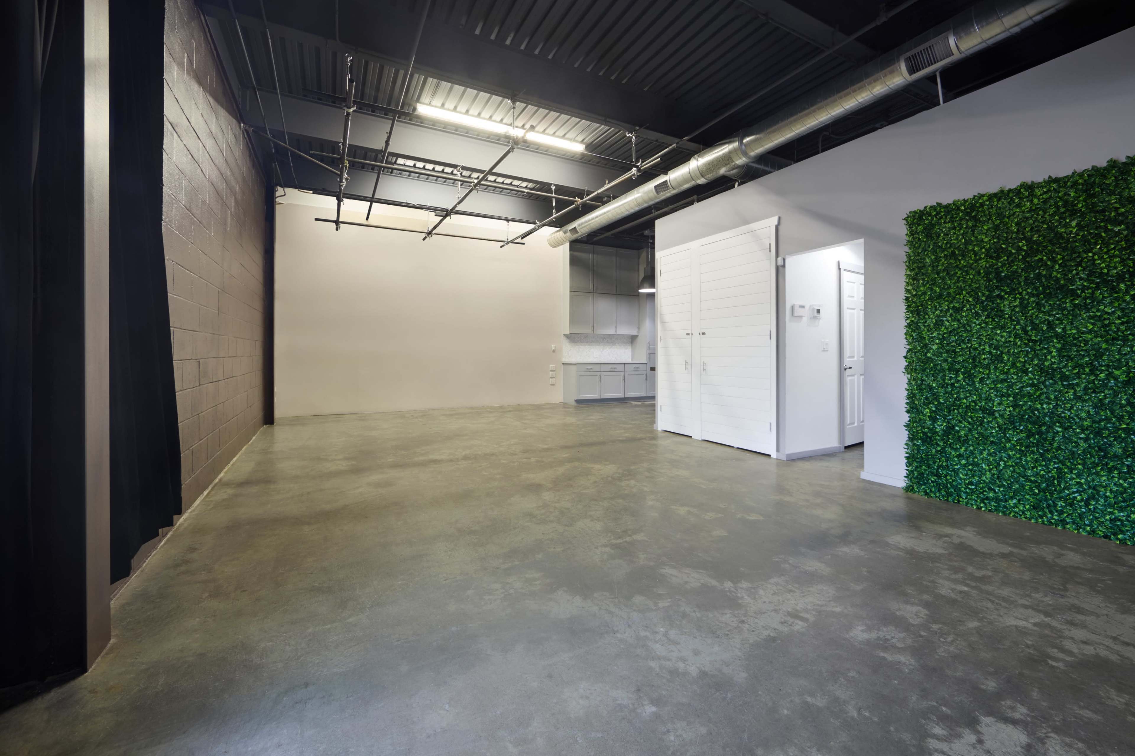 The image depicts an empty, industrial-style room with polished concrete flooring, metal beams, and a green wall feature.