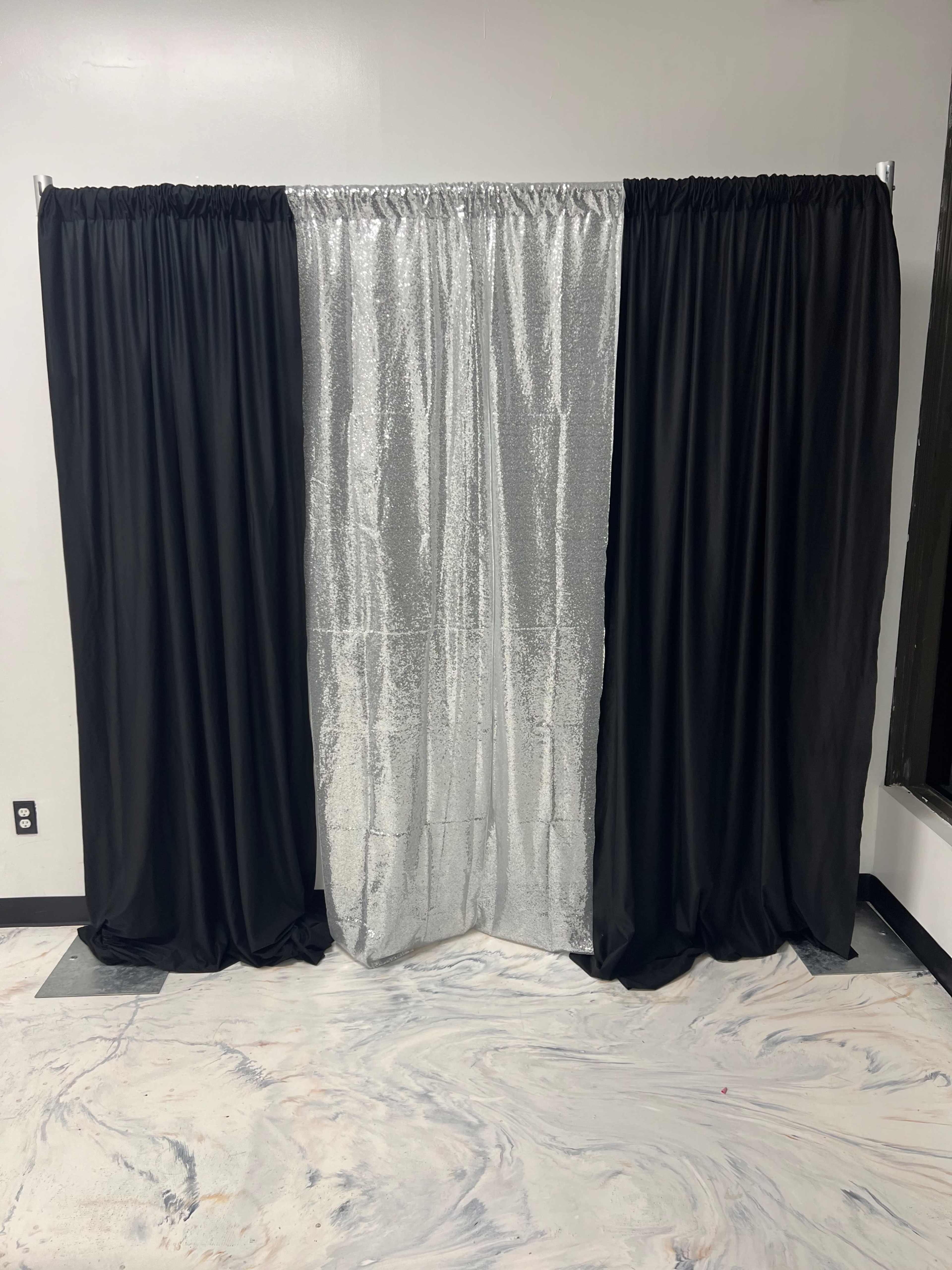 A backdrop consisting of black curtains on either side and a center panel of silver sequined material.
