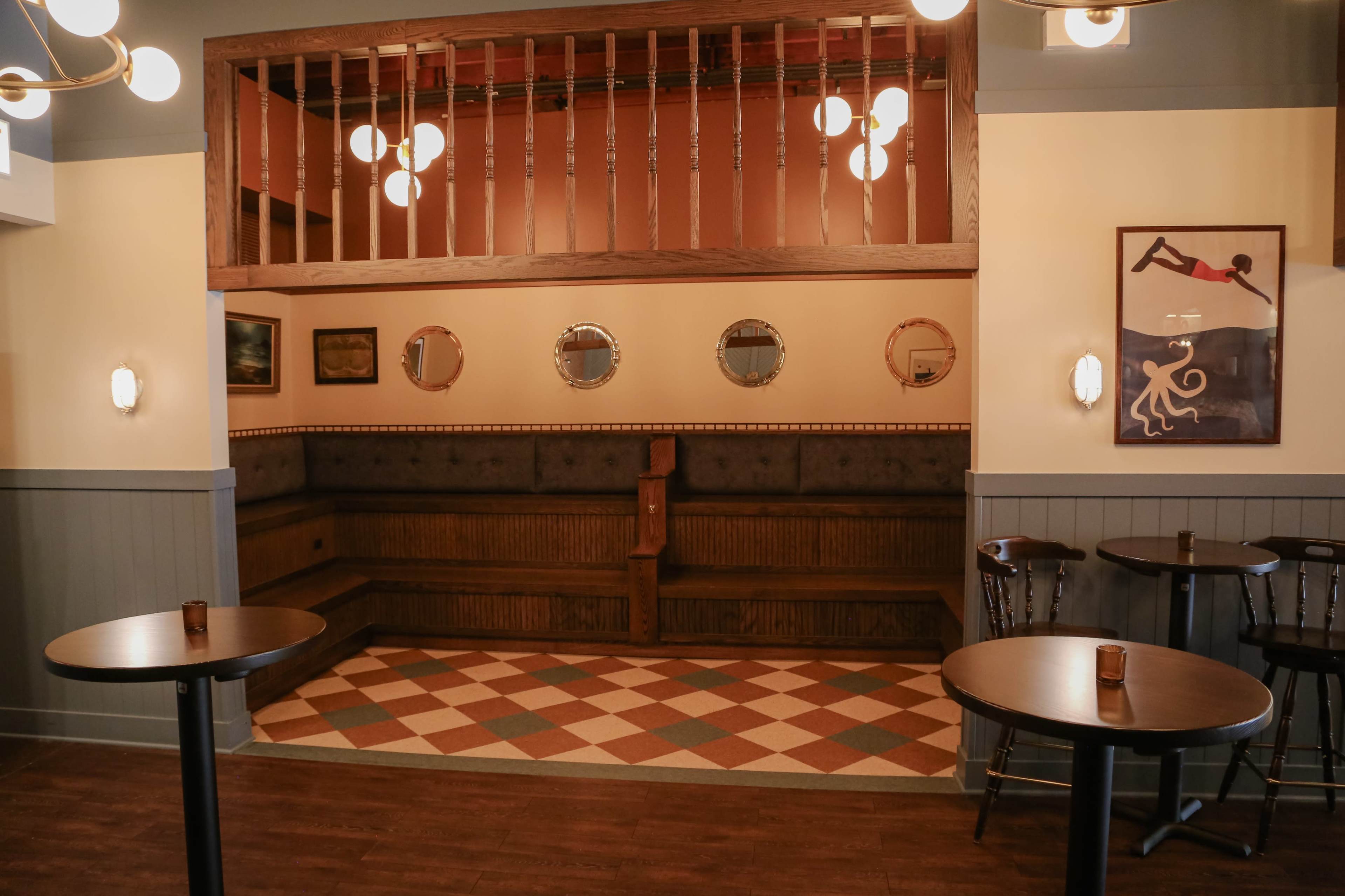 The image shows a cozy restaurant interior featuring wooden benches, round tables, and decorative wall mirrors, with a patterned rug on the floor.