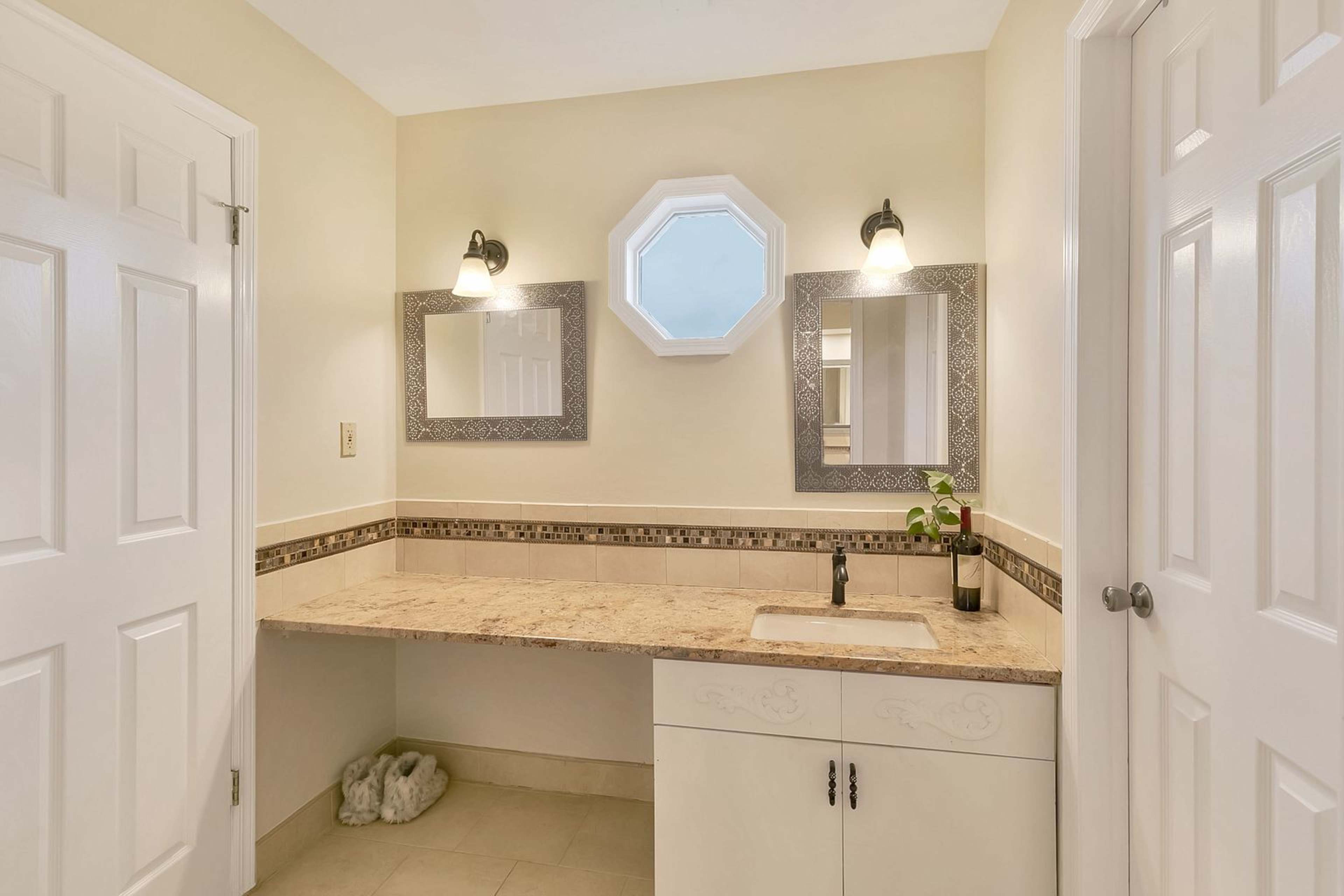 The image shows a bathroom with a countertop, two mirrors, and an octagonal window.