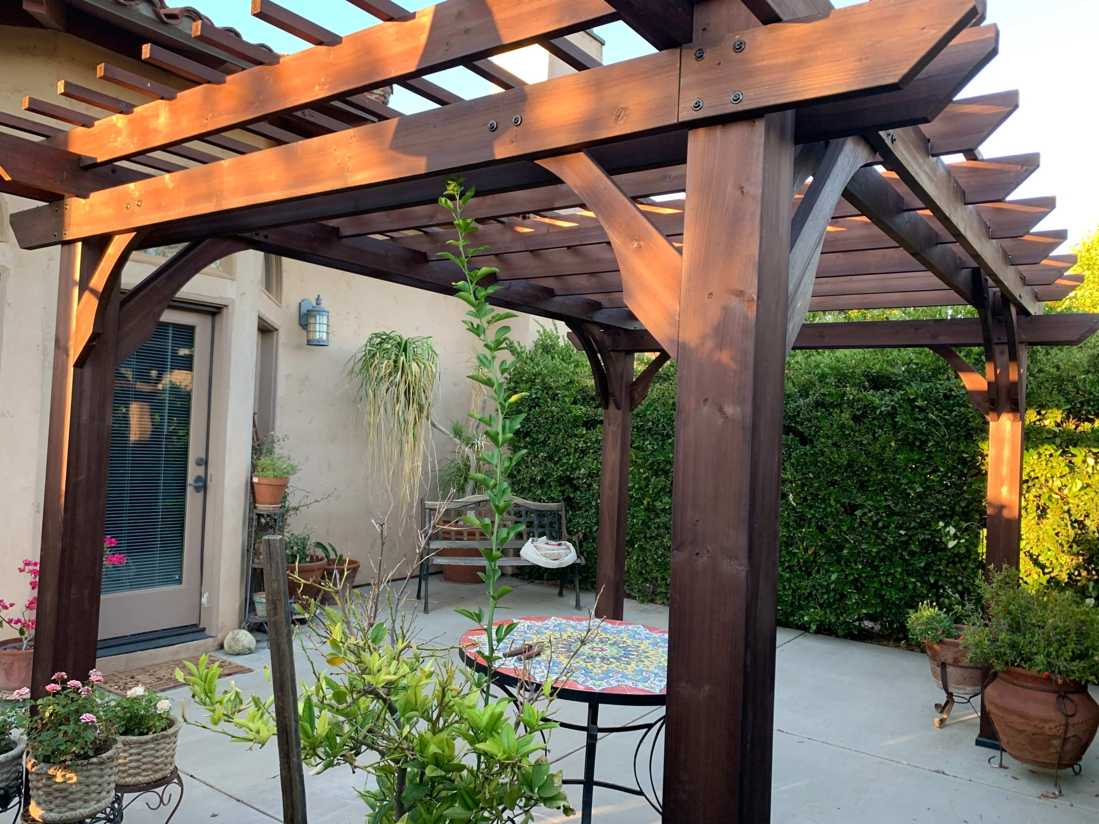 A wooden pergola shades a patio area adorned with potted plants and a round table.