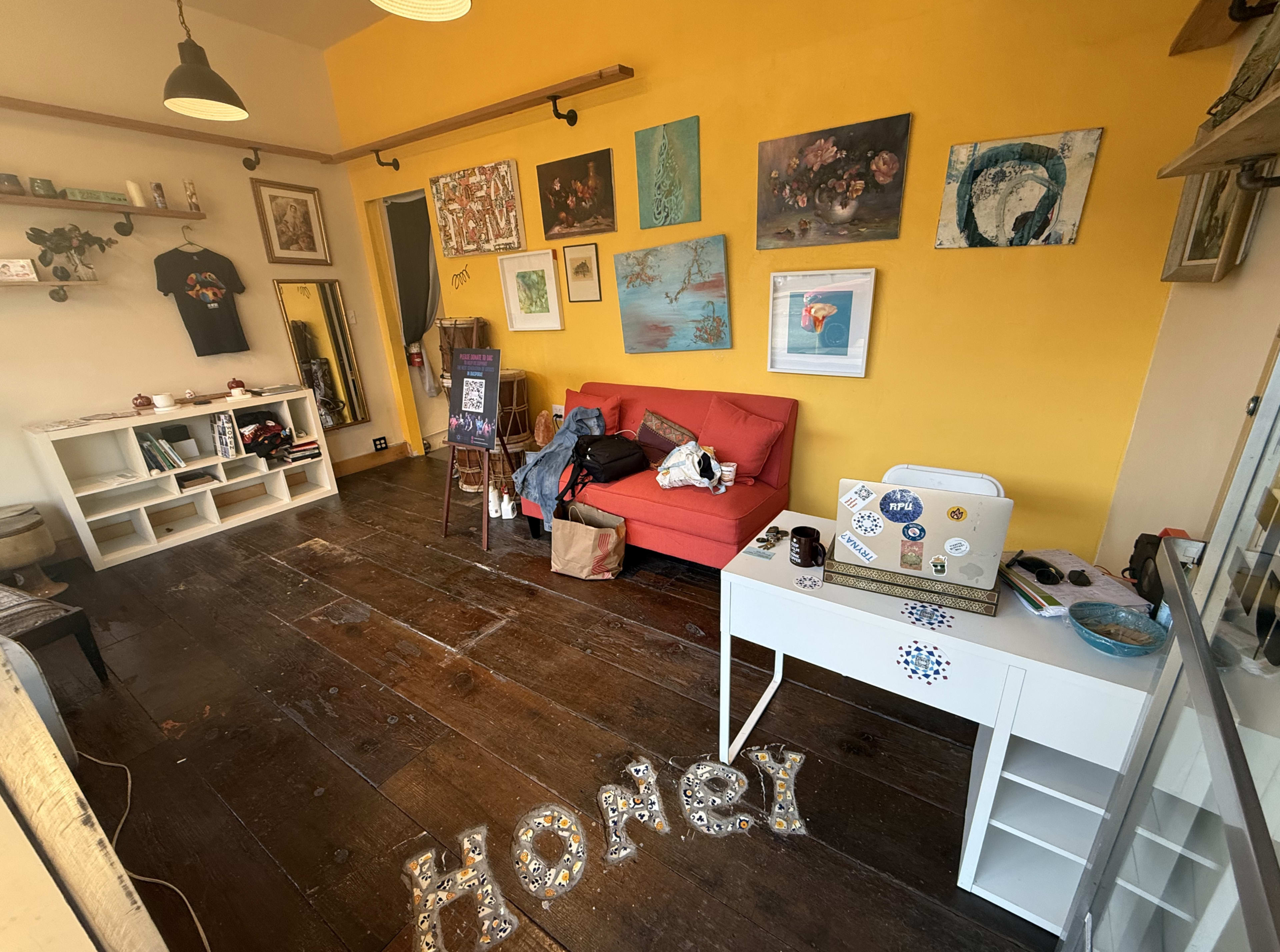 The room features a yellow wall, a red couch, various artworks hanging on the walls, and scattered items on the floor and furniture.