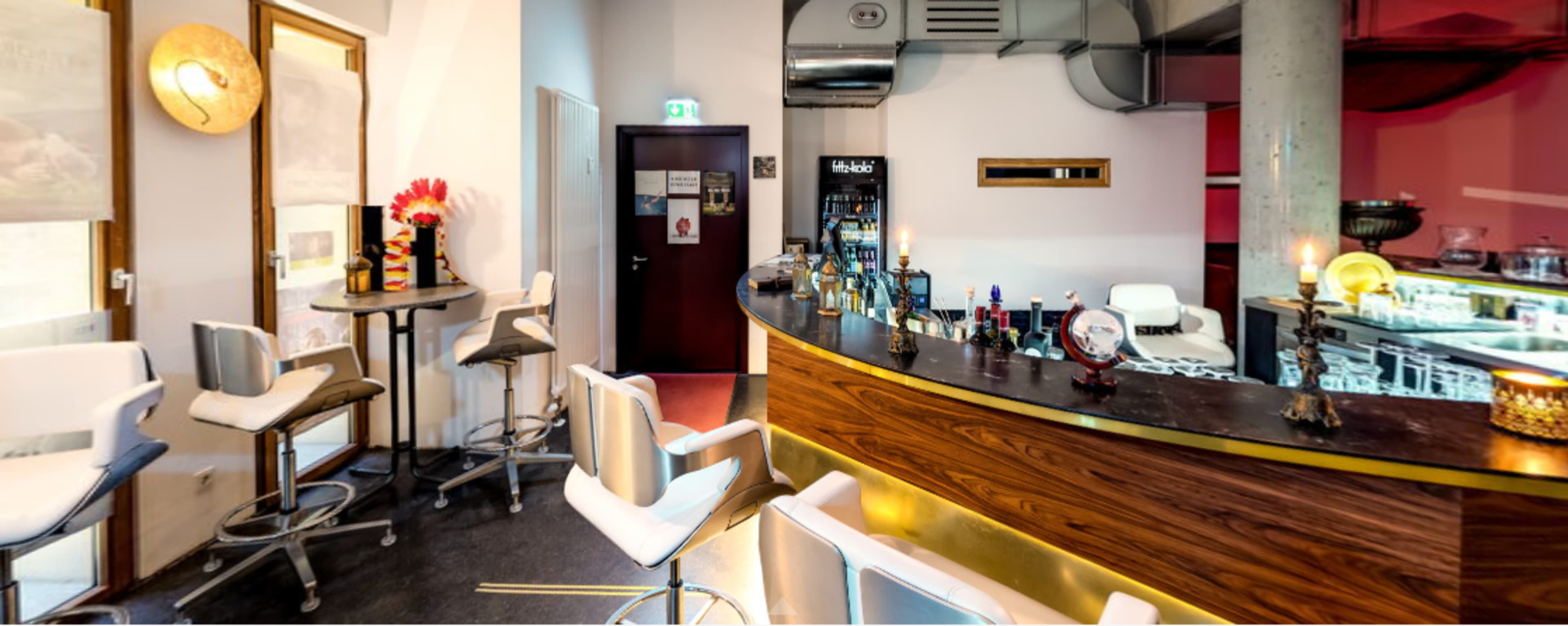 A modern bar area with a curved wooden counter, high stools, and a few tables, surrounded by minimalist decor.
