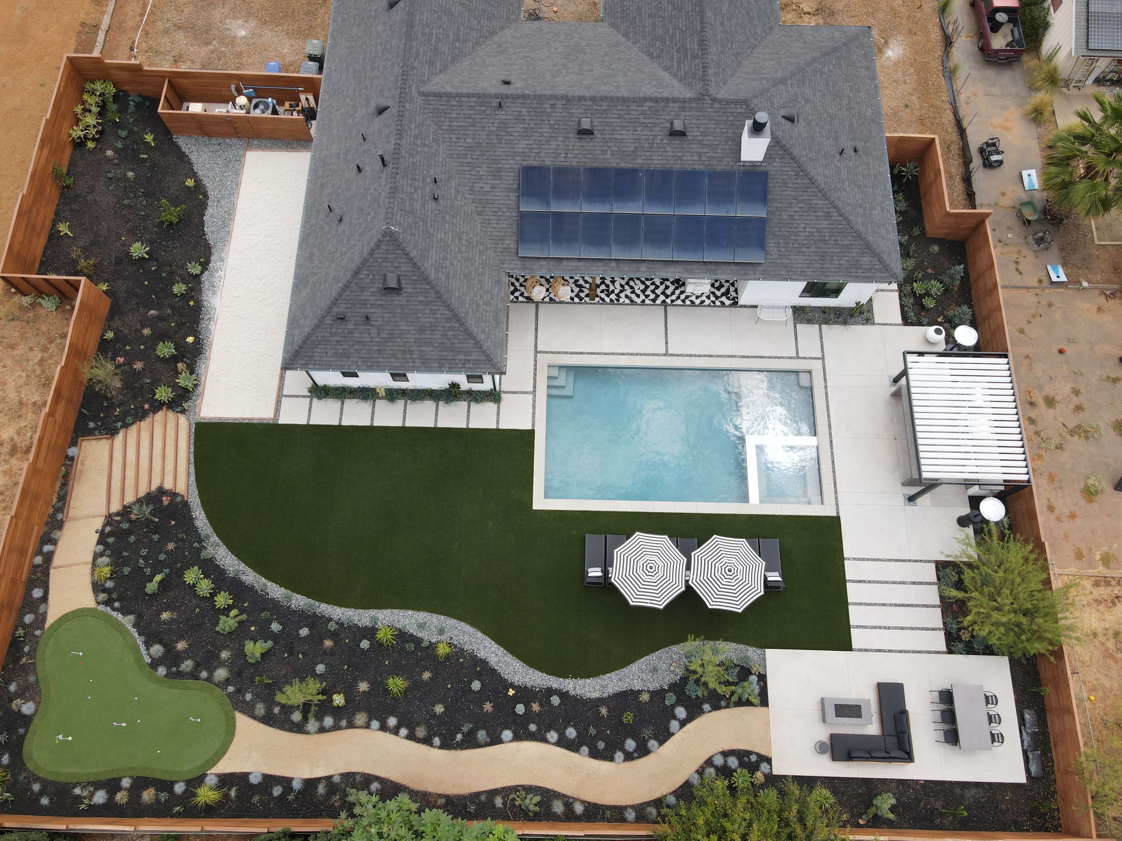 An aerial view of a residential backyard featuring a swimming pool, a landscaped garden with a putting green, and multiple seating areas.