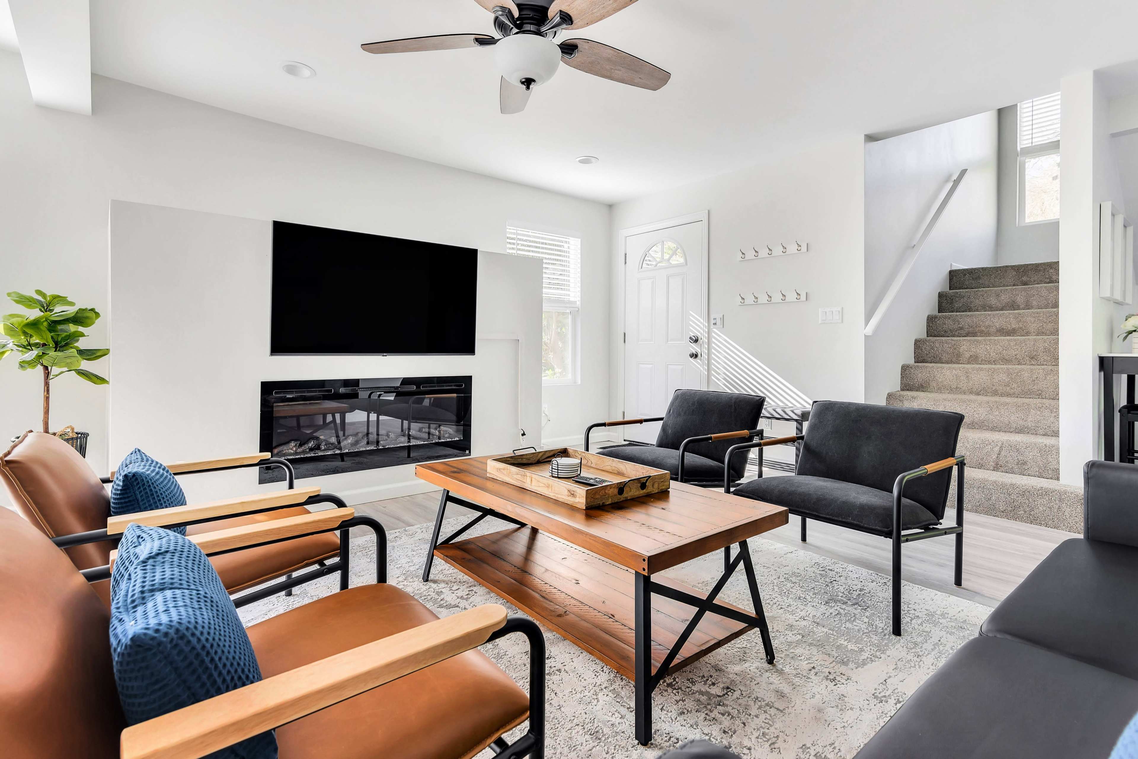 The living room features a modern design with a television mounted on the wall, a wooden coffee table, and seating arranged around it, along with stairs leading to a second level.