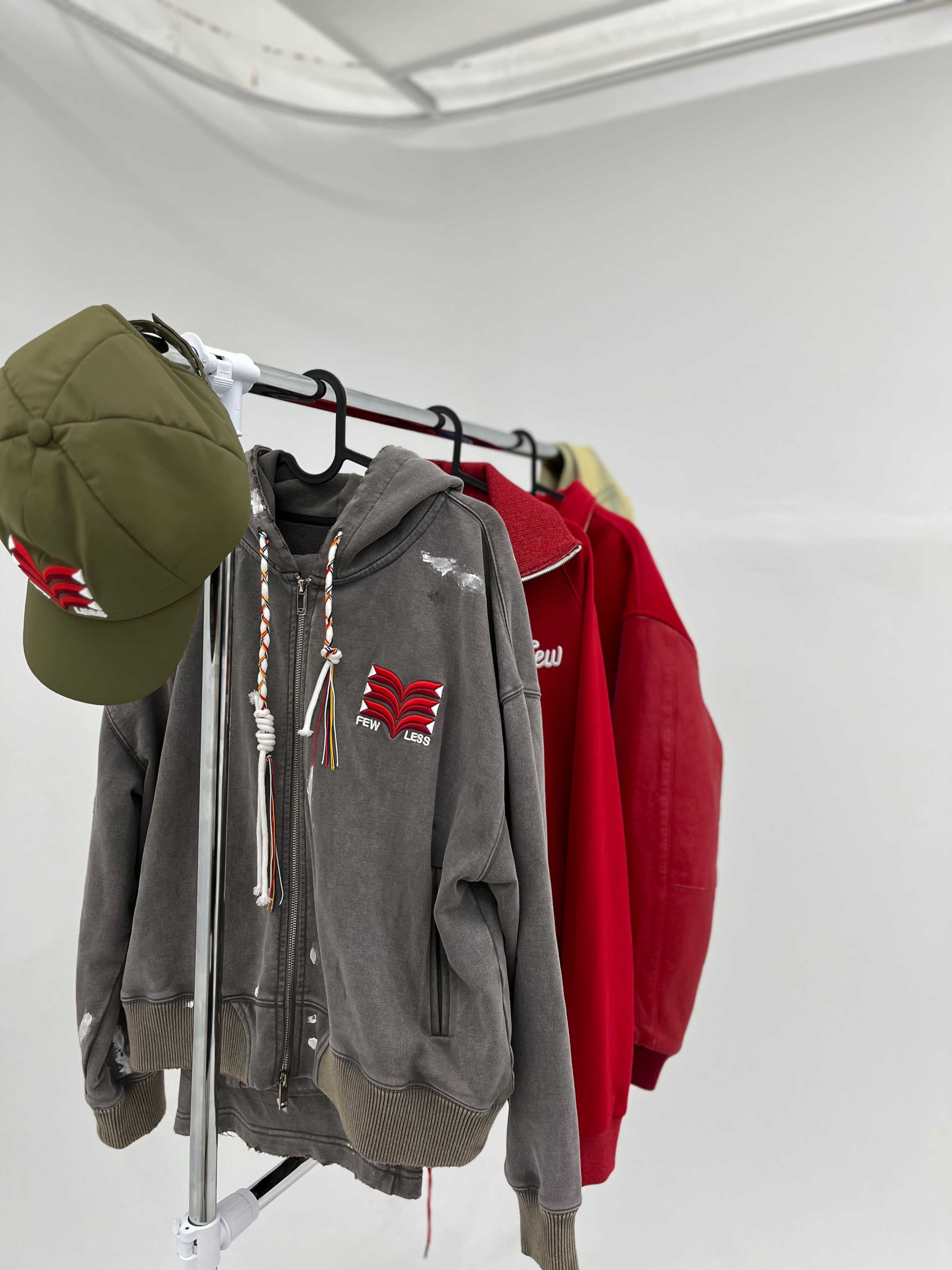 A clothing rack displays a gray zip-up hoodie, a red sweatshirt, and a green cap.