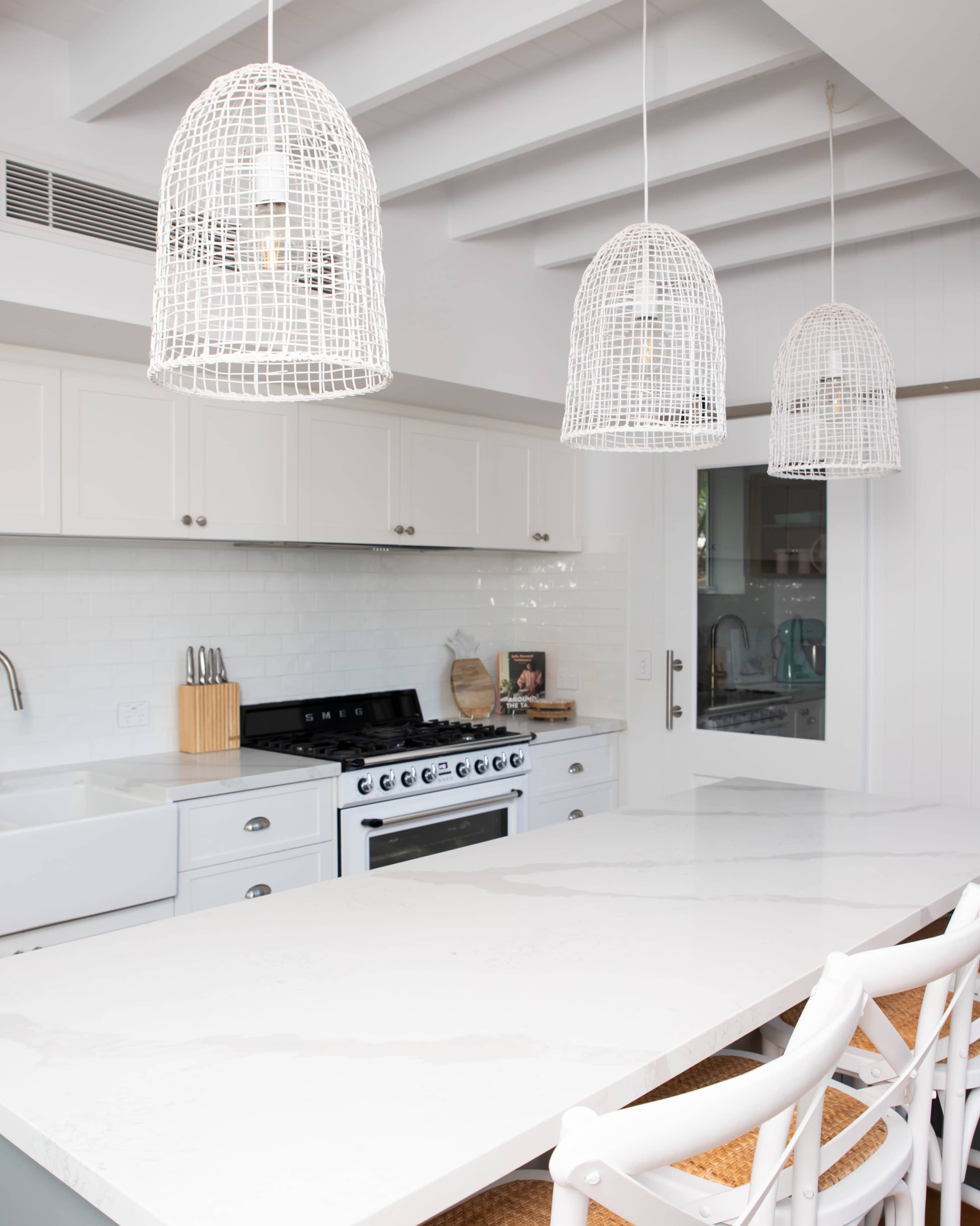 A modern kitchen features a large white marble island, three woven pendant lights, and stainless steel appliances.