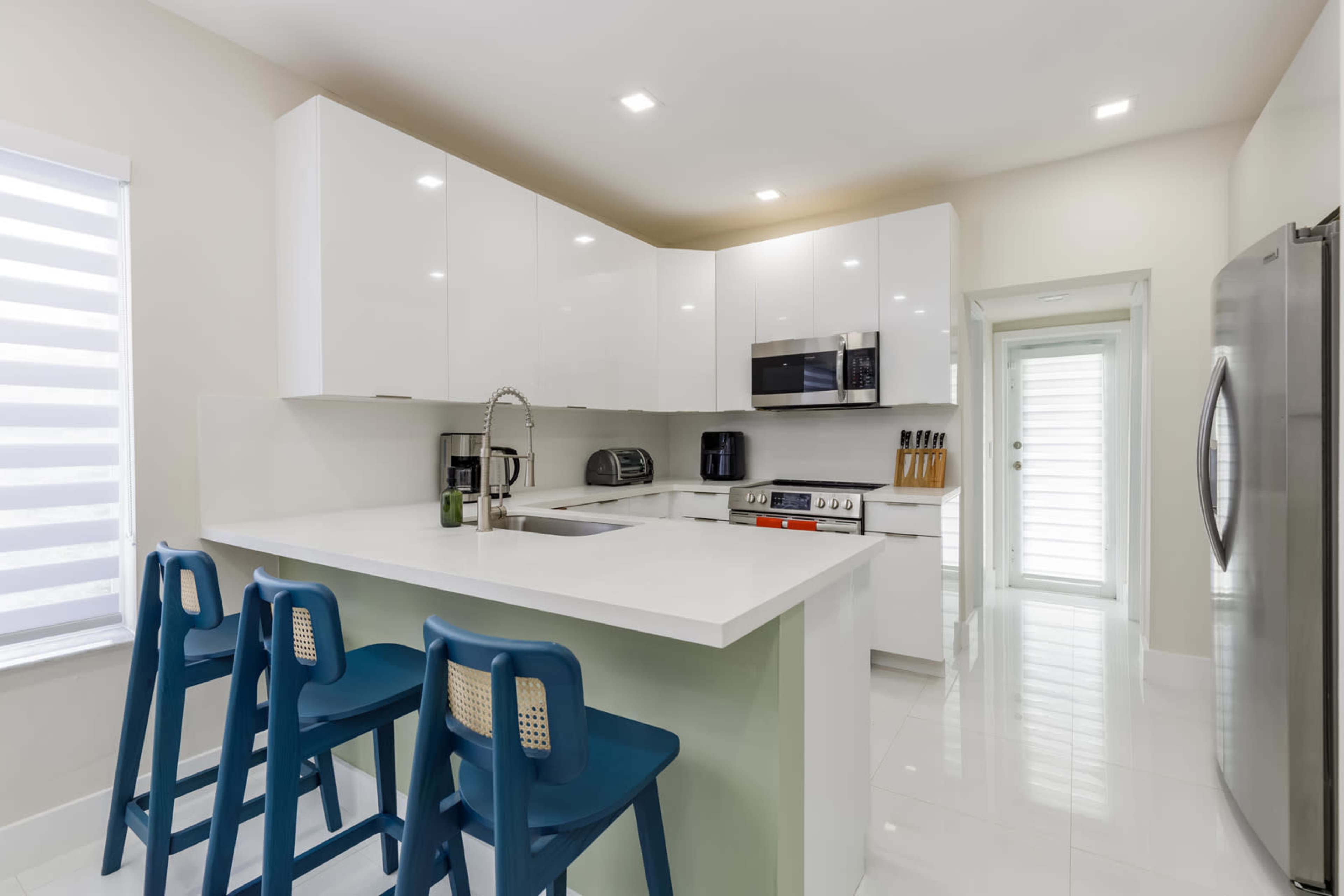 A modern kitchen features white cabinetry, stainless steel appliances, a large island with seating, and a glass door leading to an outdoor area.