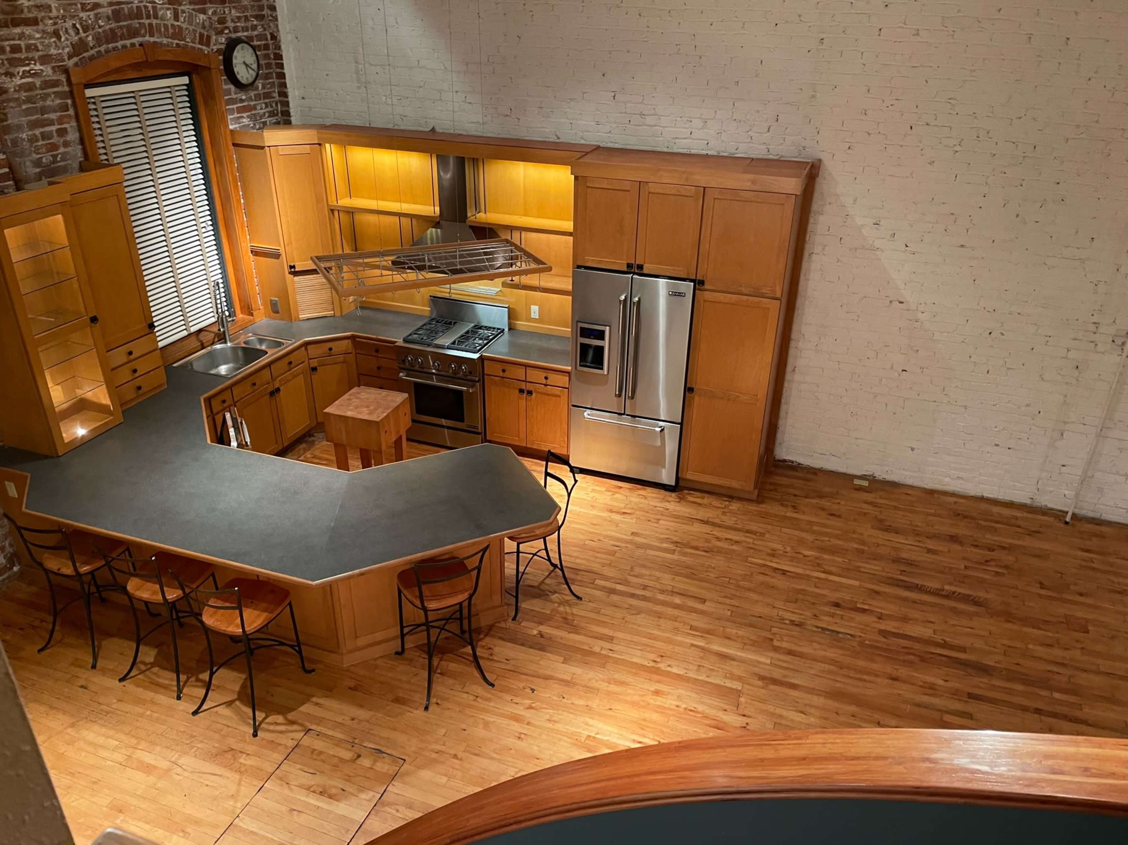 A spacious kitchen with wooden cabinets, a large island with bar seating, and modern appliances against a backdrop of exposed brick walls and hardwood floors.