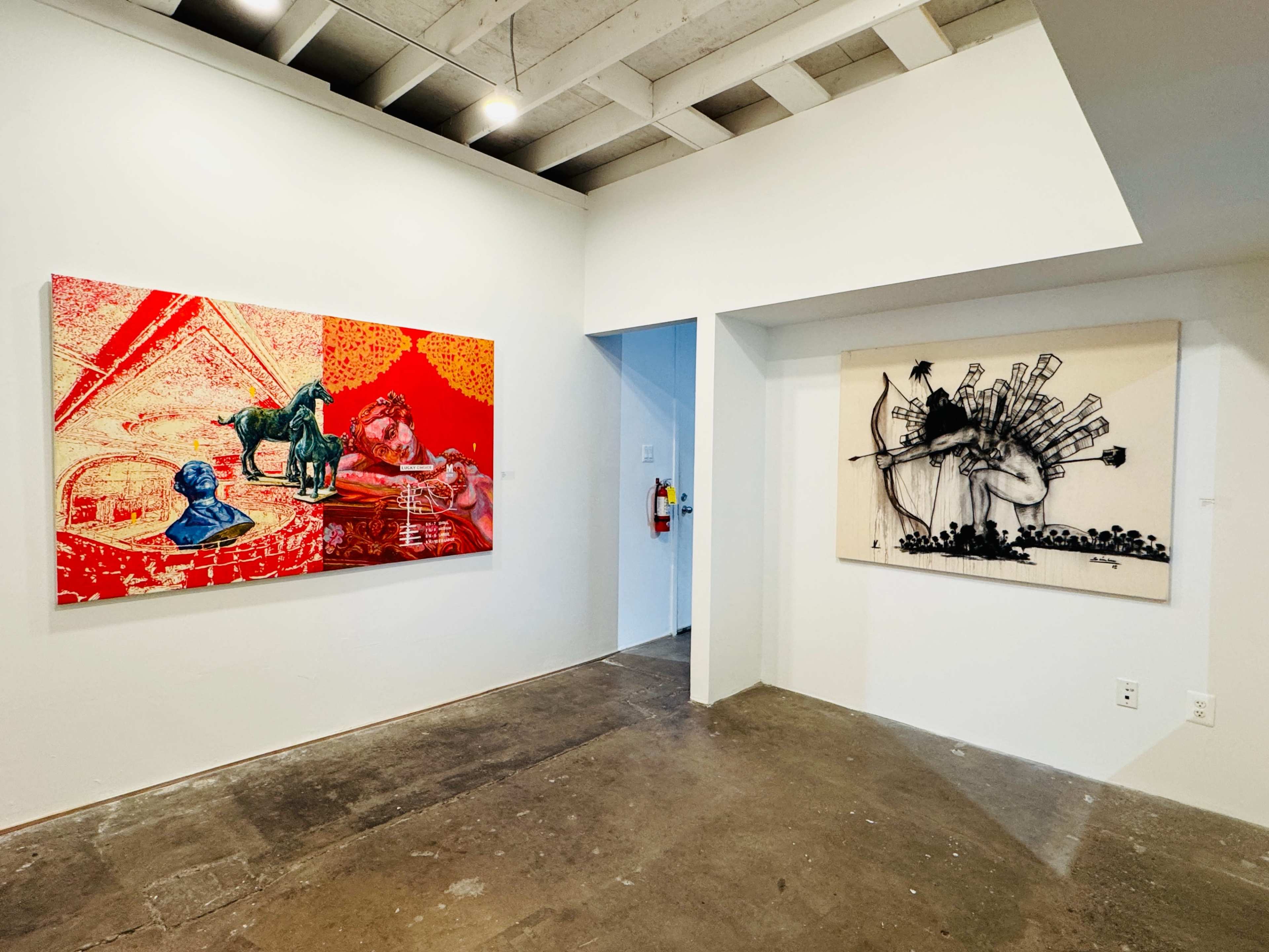 The image shows an indoor art gallery with two contrasting wall artworks, one vibrant and colorful and the other monochromatic and abstract.