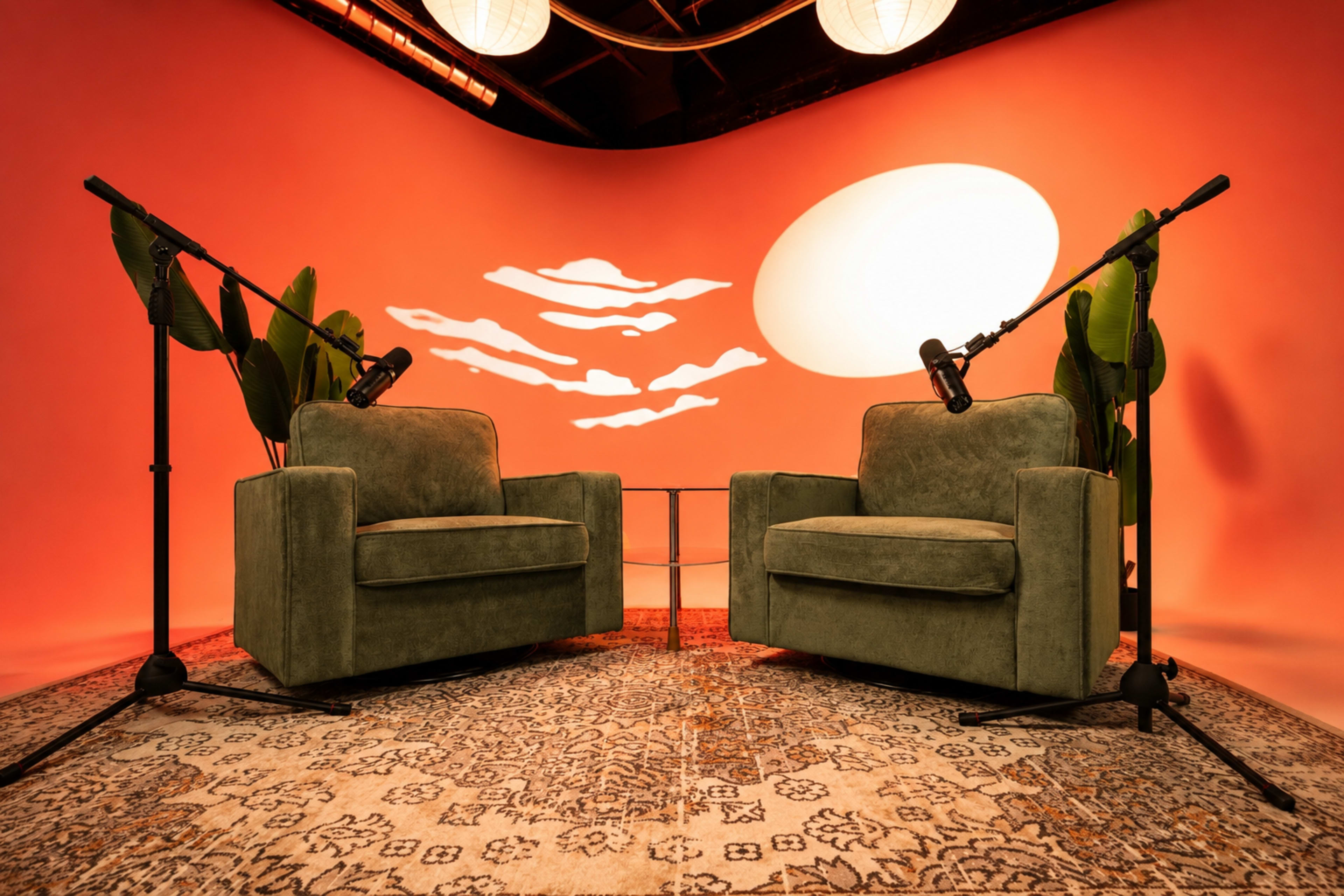 The image features two green armchairs facing each other, positioned on a patterned rug beneath a vibrant orange backdrop with a large round shape and stylized clouds.