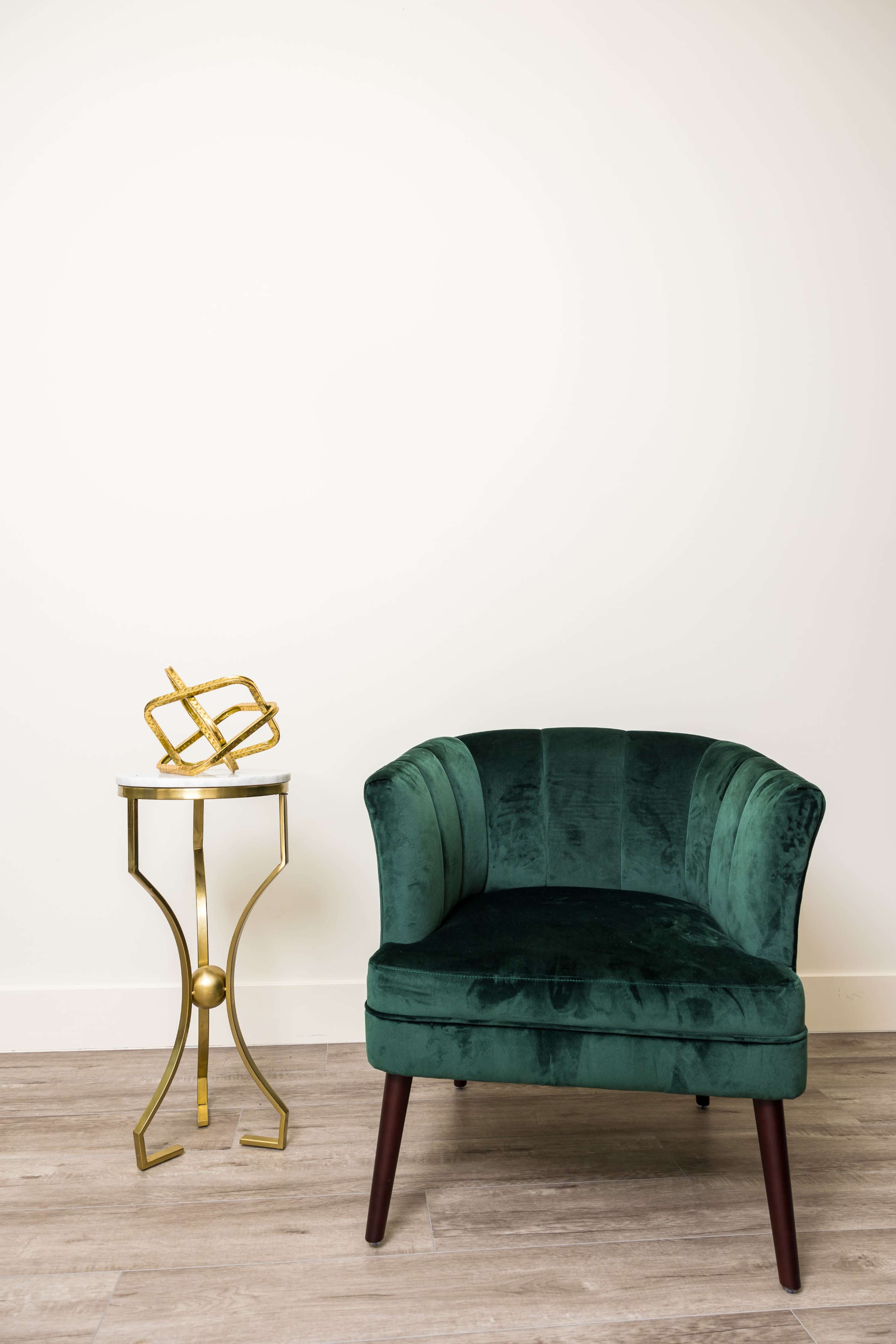 A green upholstered chair sits next to a gold side table featuring a decorative sculpture.