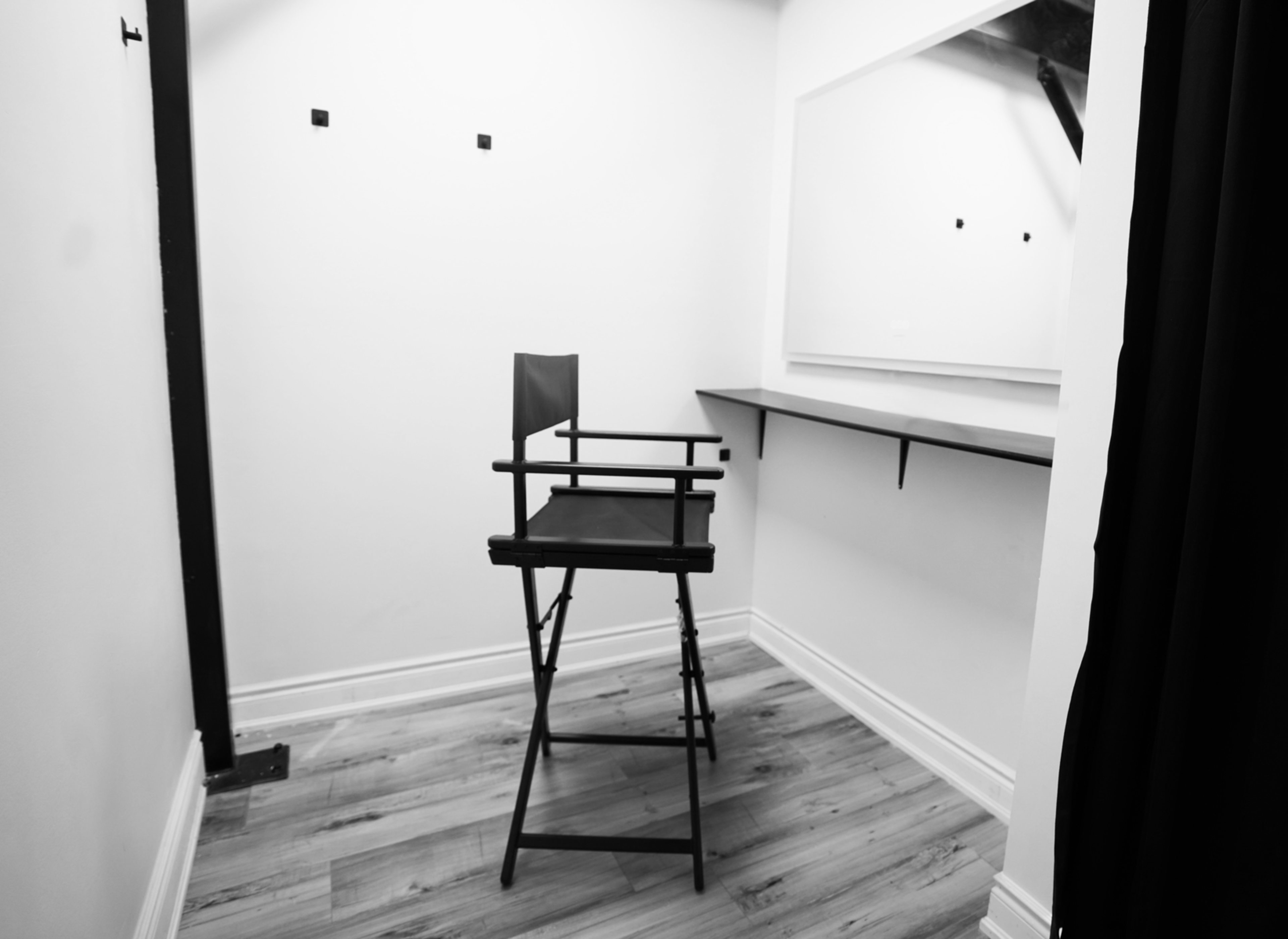 A black director's chair placed in a minimalist, empty dressing room with a wall-mounted mirror and a simple tabletop.