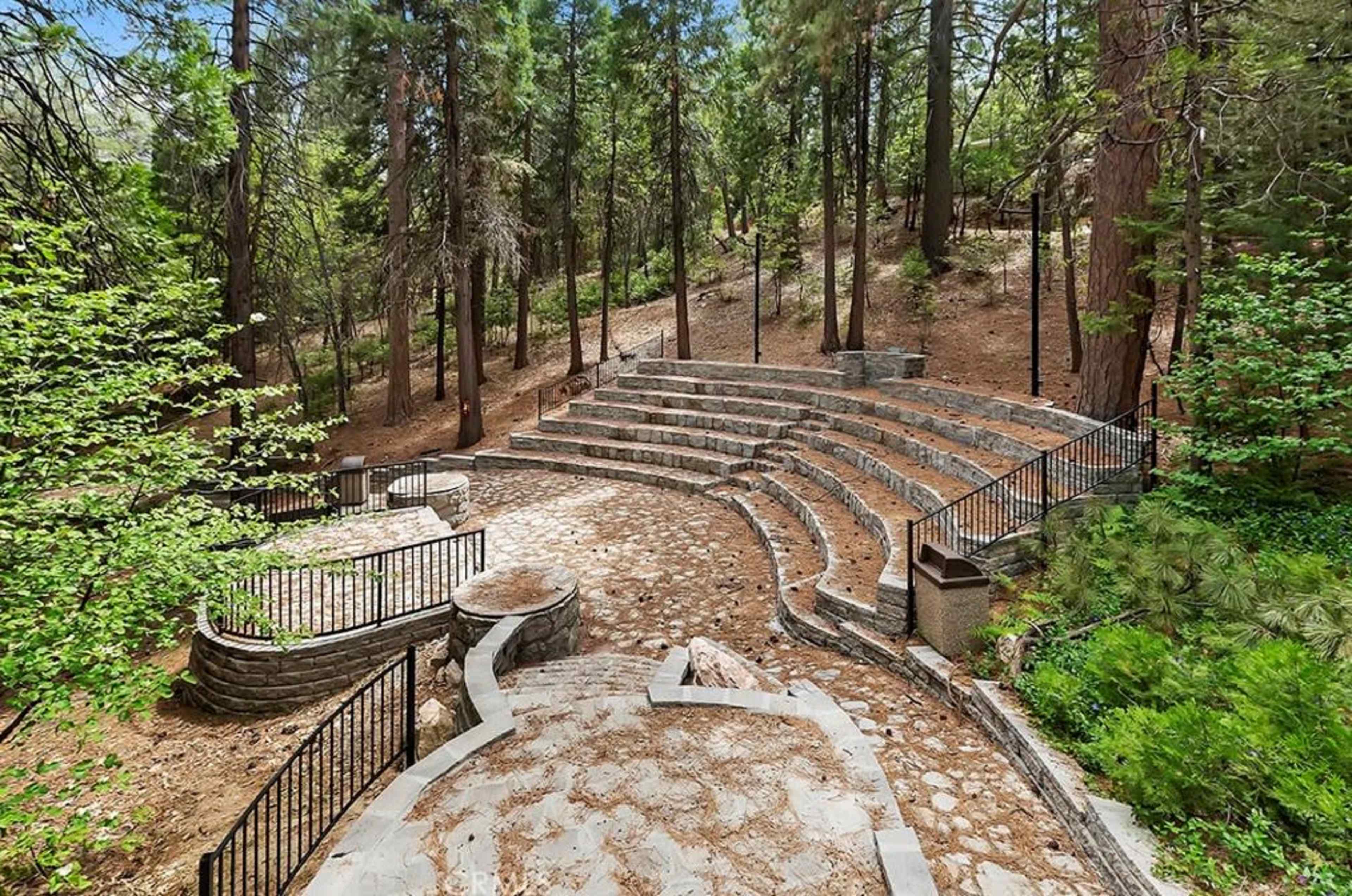 The image shows a stone amphitheater surrounded by trees in a forested area.