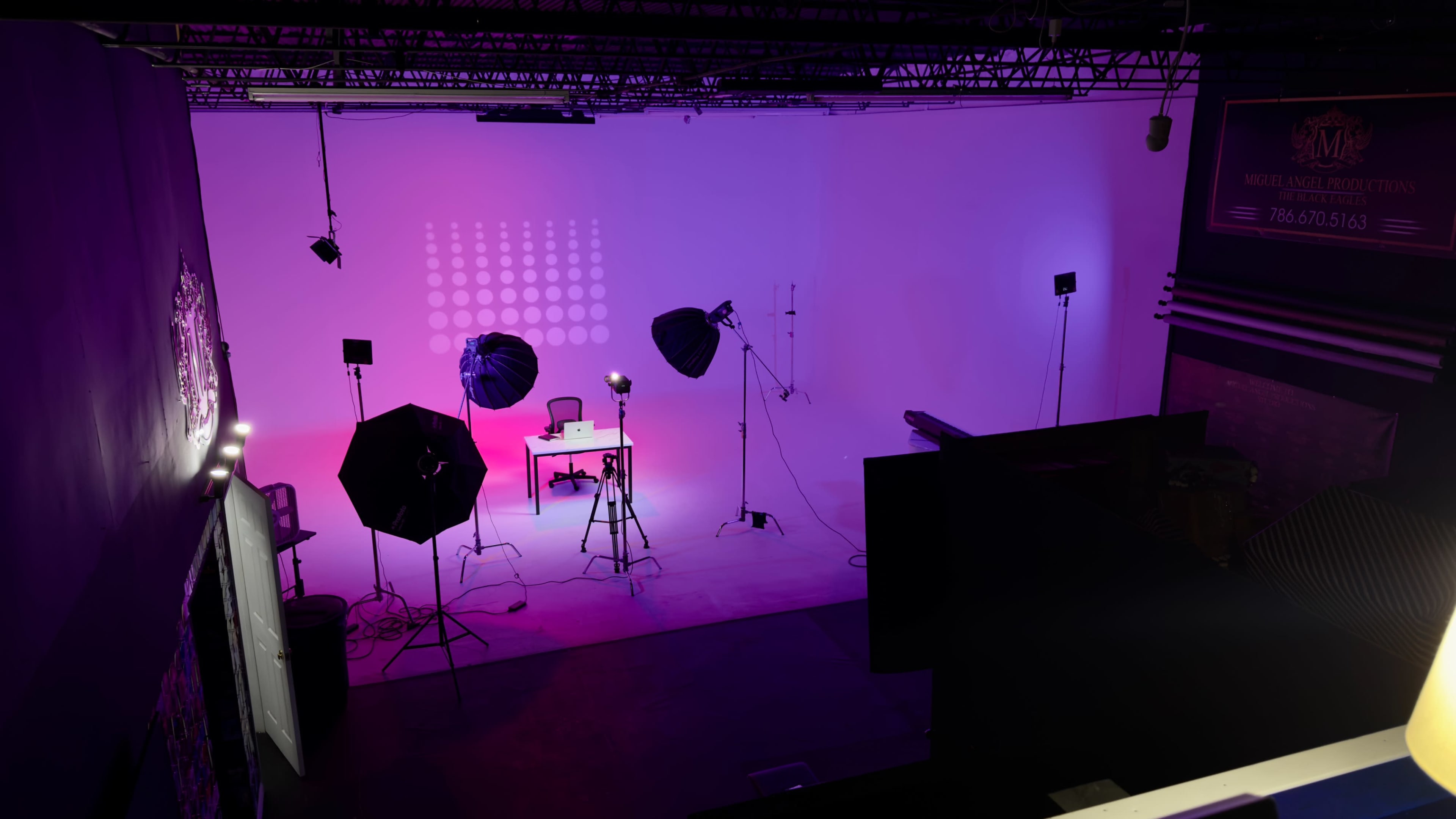 A photography studio is illuminated with colorful lights, featuring a table and a chair in the center surrounded by various lighting equipment.