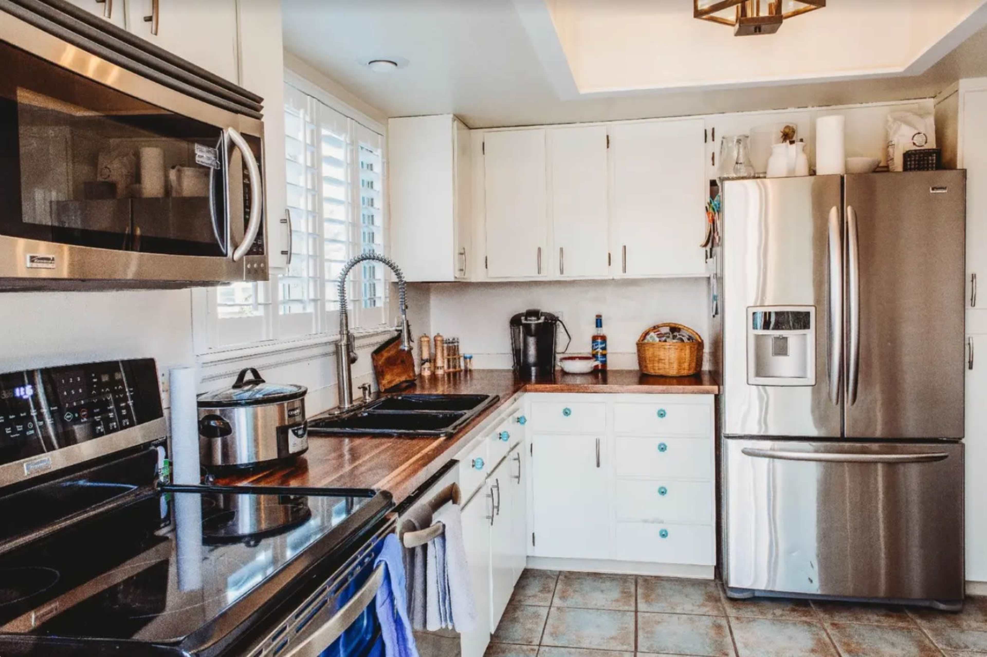 A modern kitchen features stainless steel appliances, white cabinetry with teal knobs, and a wooden countertop.