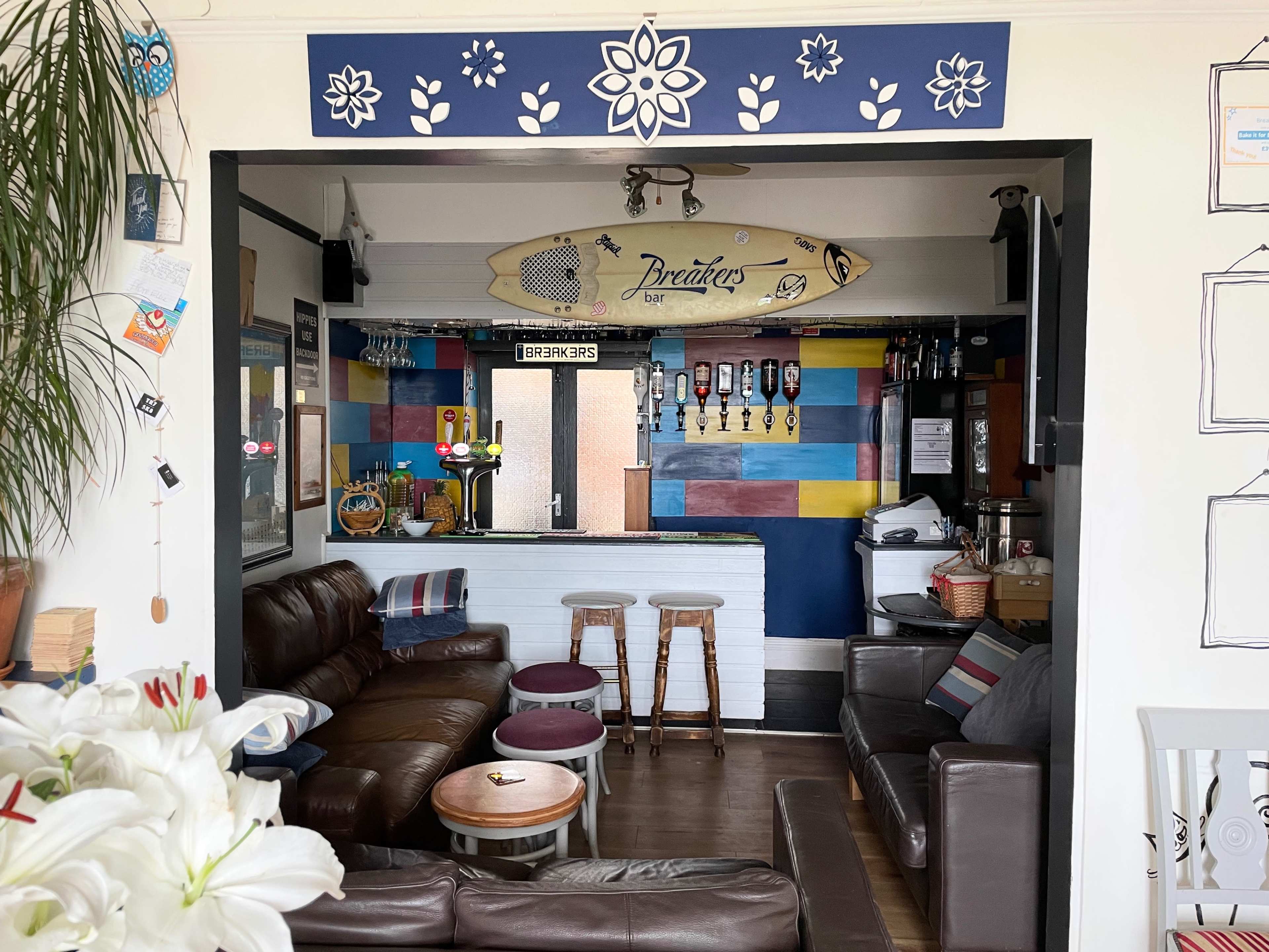 A cozy bar area featuring a surfboard, colorful wall decor, and comfortable seating.