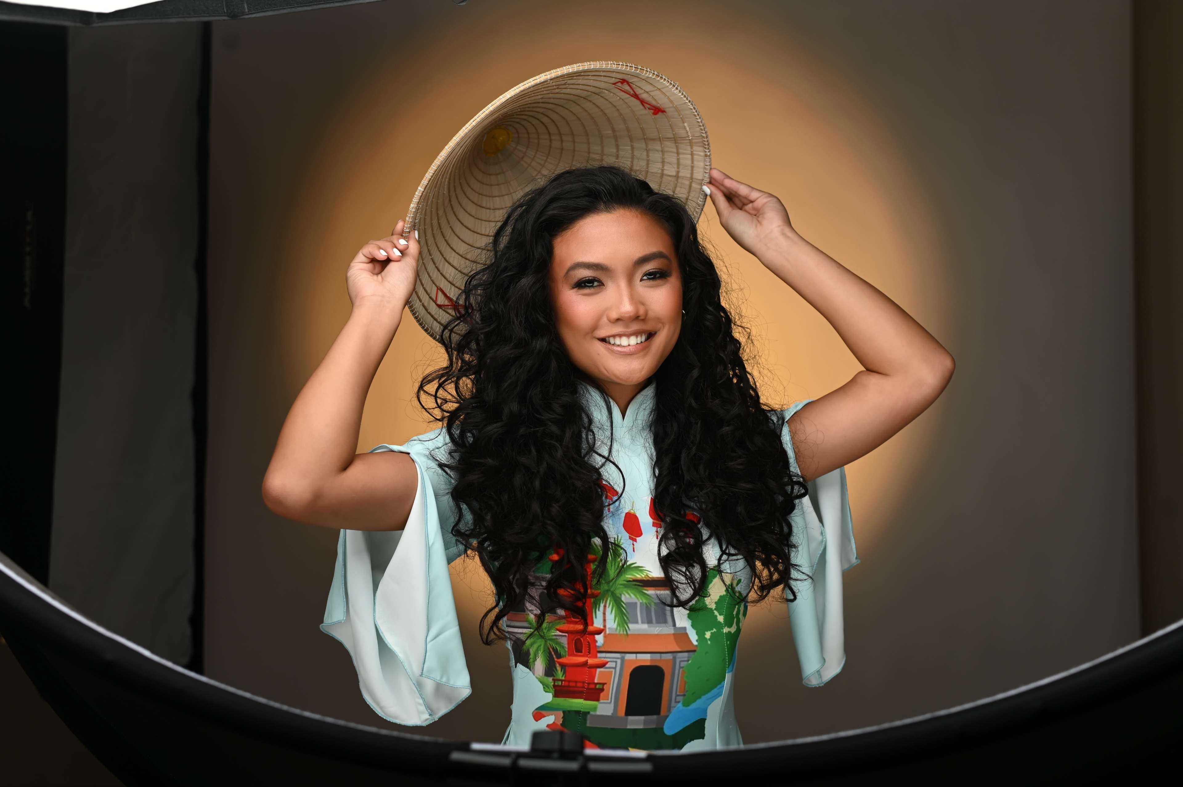A woman wearing a traditional outfit and a large straw hat poses for a photo with soft lighting in the background.
