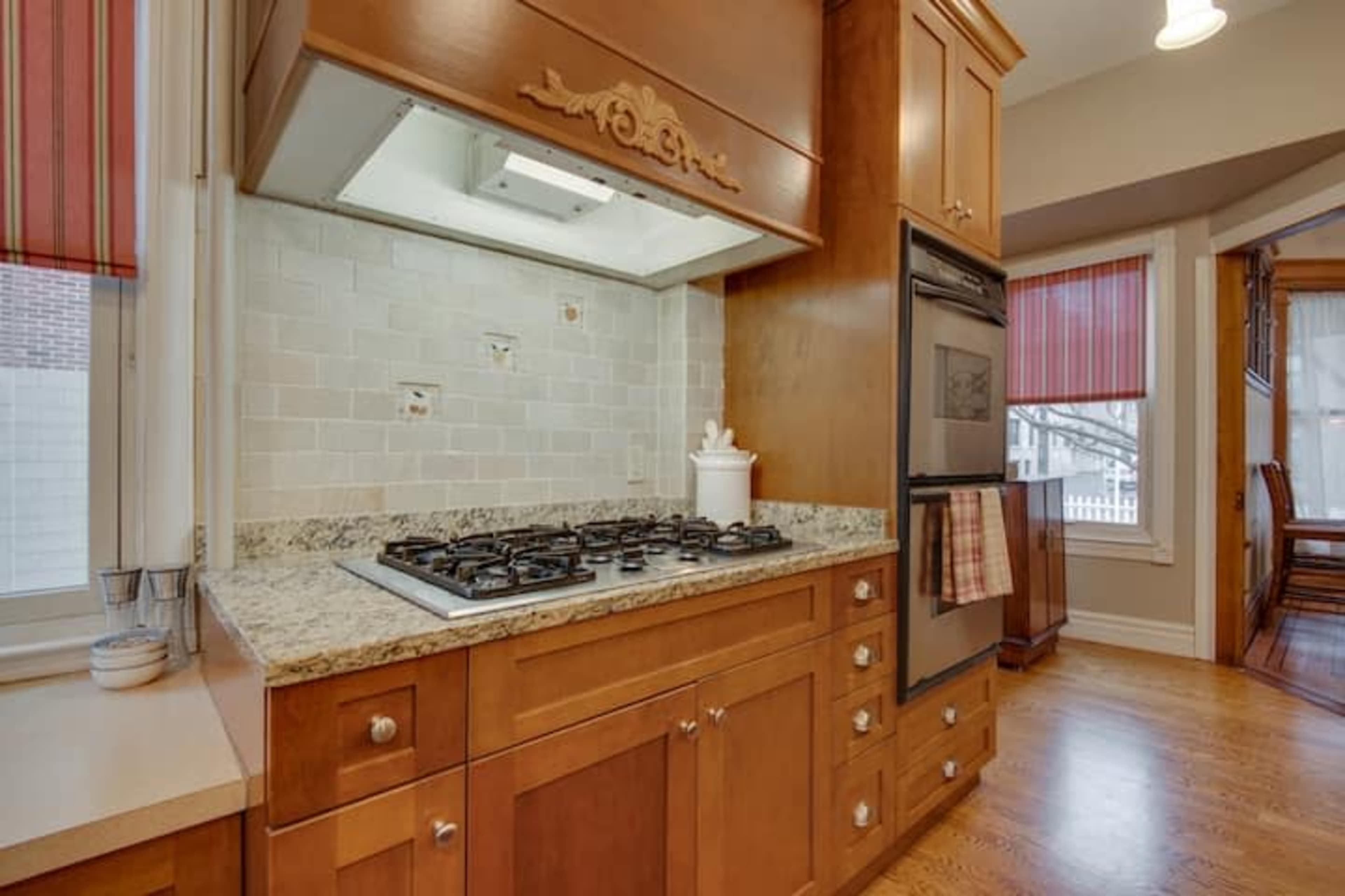 A kitchen featuring a gas stove, a double oven, wooden cabinetry, and a backsplash with light-colored tiles.