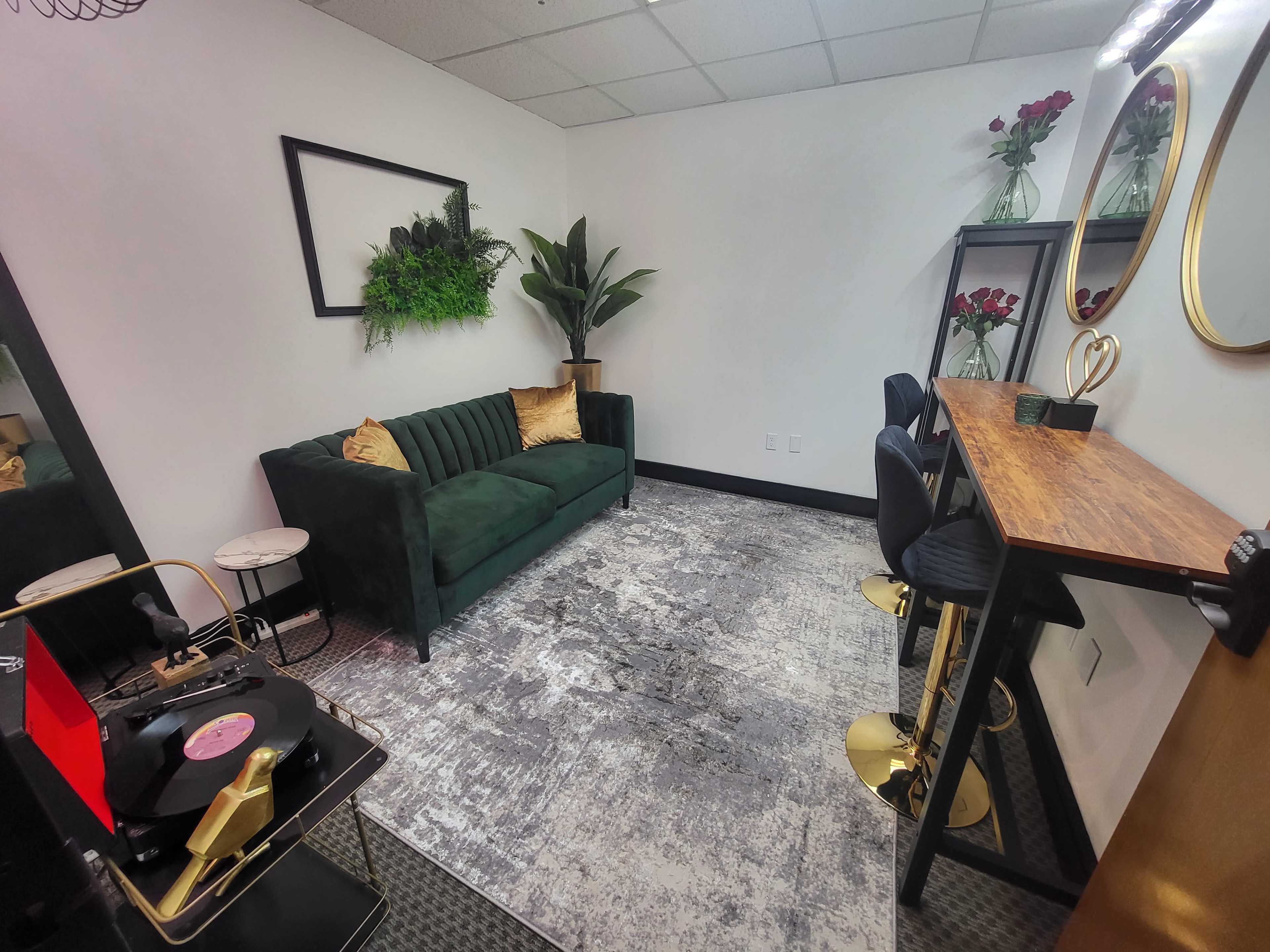 A small, modern room featuring a green sofa, a wooden table with black stools, and decorative plants along with a record player in the corner.