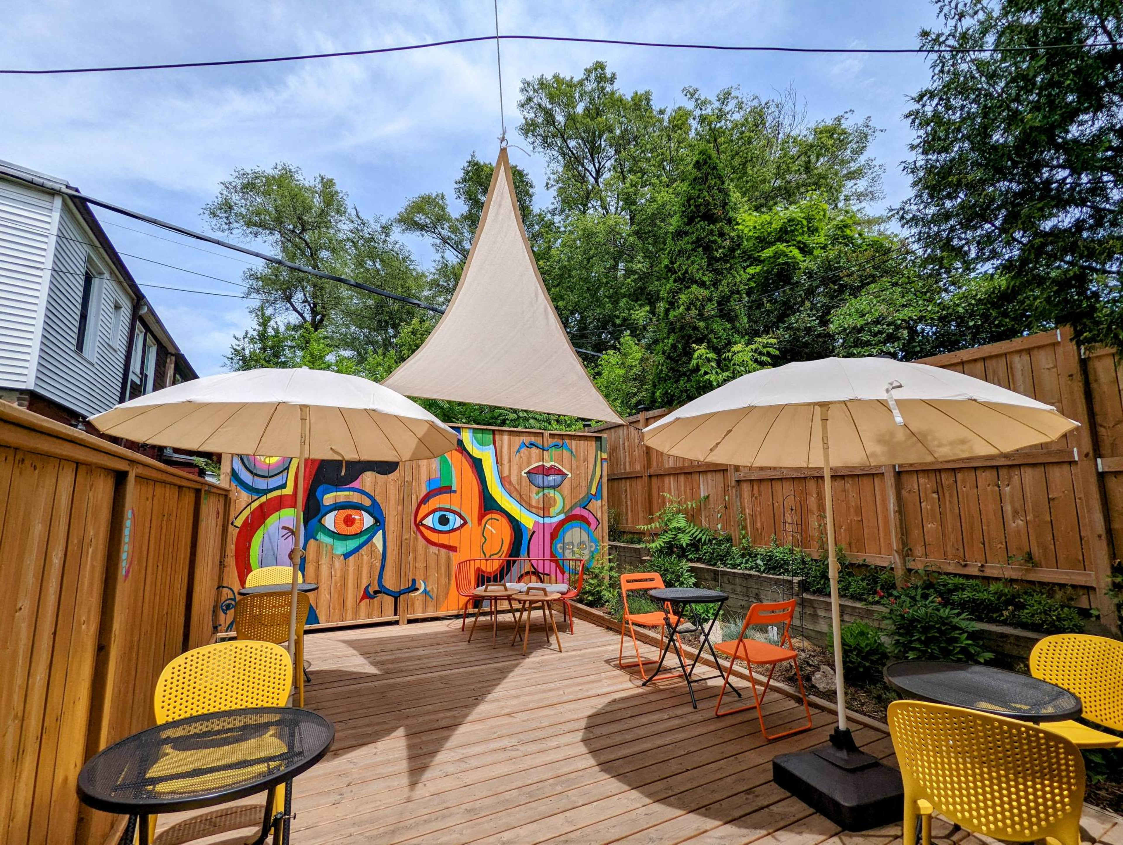 A vibrant outdoor patio features colorful murals, two large umbrellas, and a wooden deck surrounded by greenery.