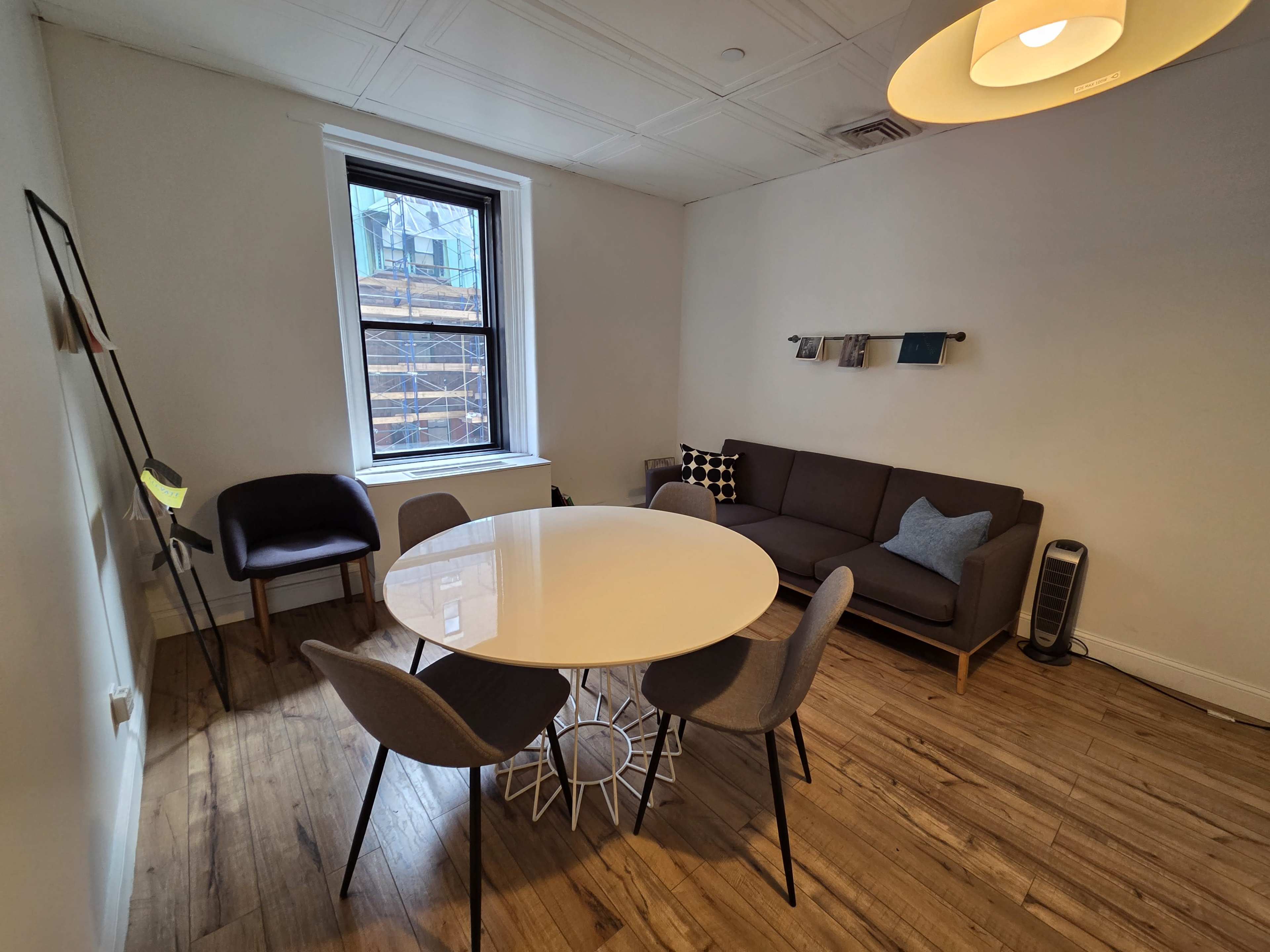 The image shows a modern, minimalistic room with a round white table surrounded by four chairs, a gray sofa, and a lamp near the wall.