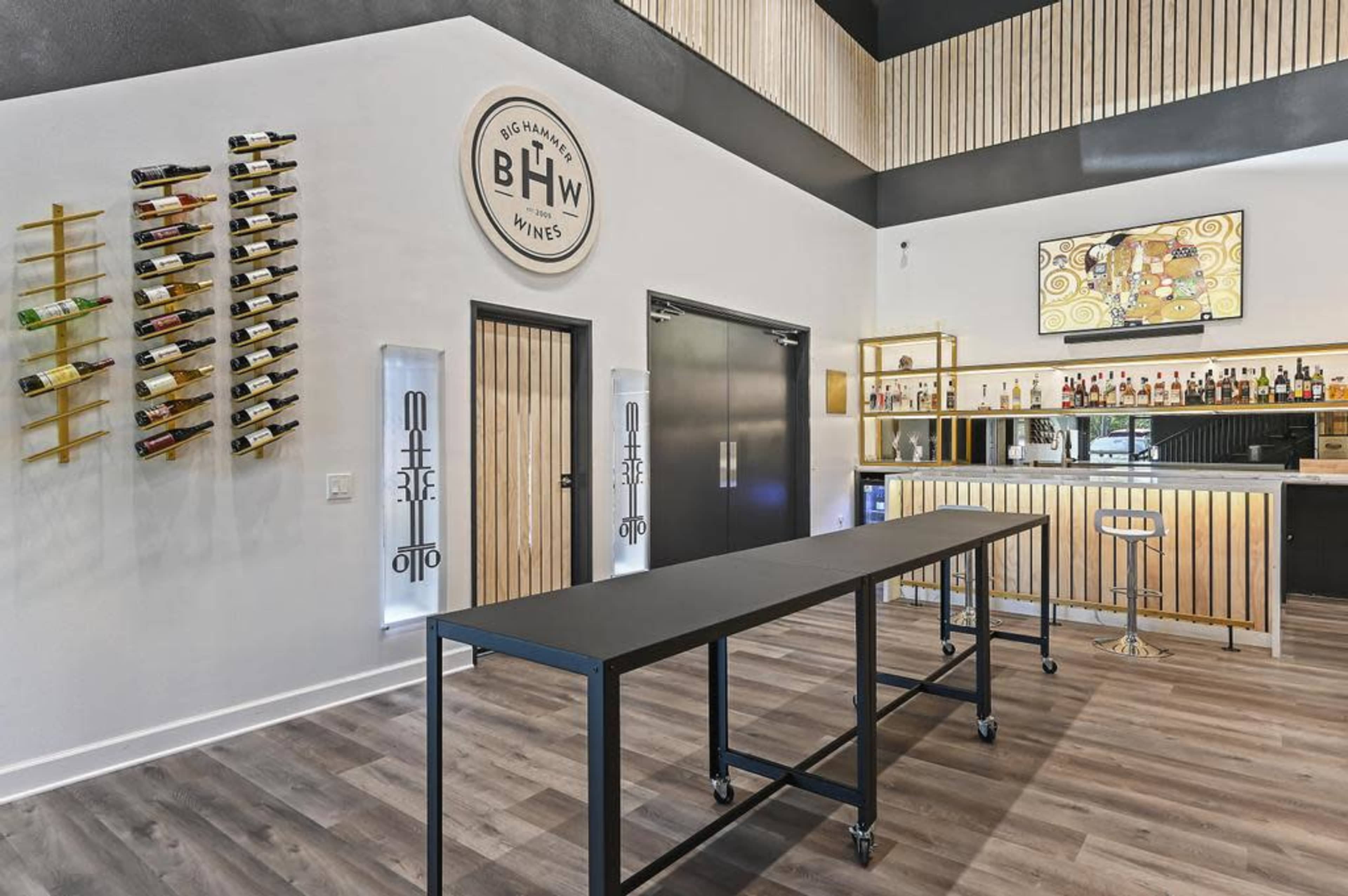 The image shows a modern wine tasting room with a sleek bar, wine racks on the wall, and contemporary decor.
