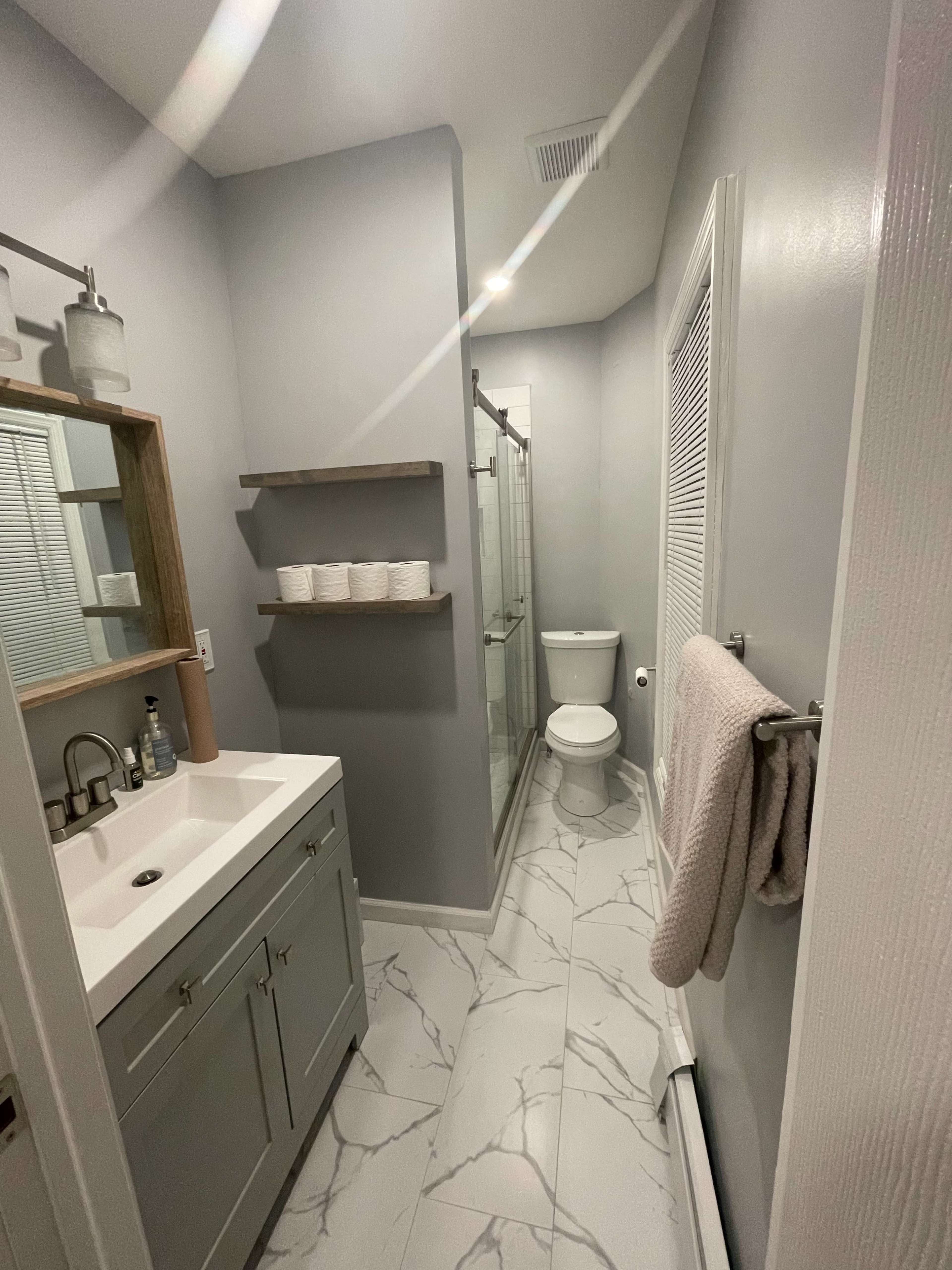 A modern bathroom featuring gray walls, a glass shower, a toilet, a sink with a vanity, and neatly arranged towels on a wall hook.