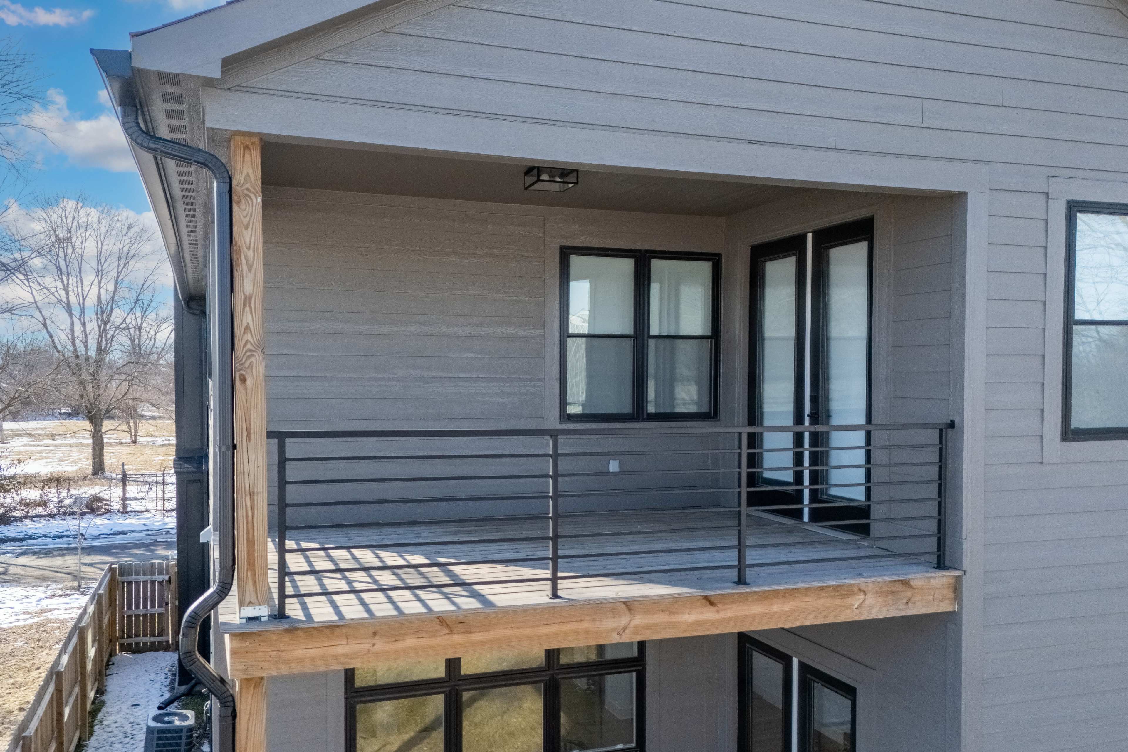 The image shows a balcony of a house featuring wooden flooring and a black railing.