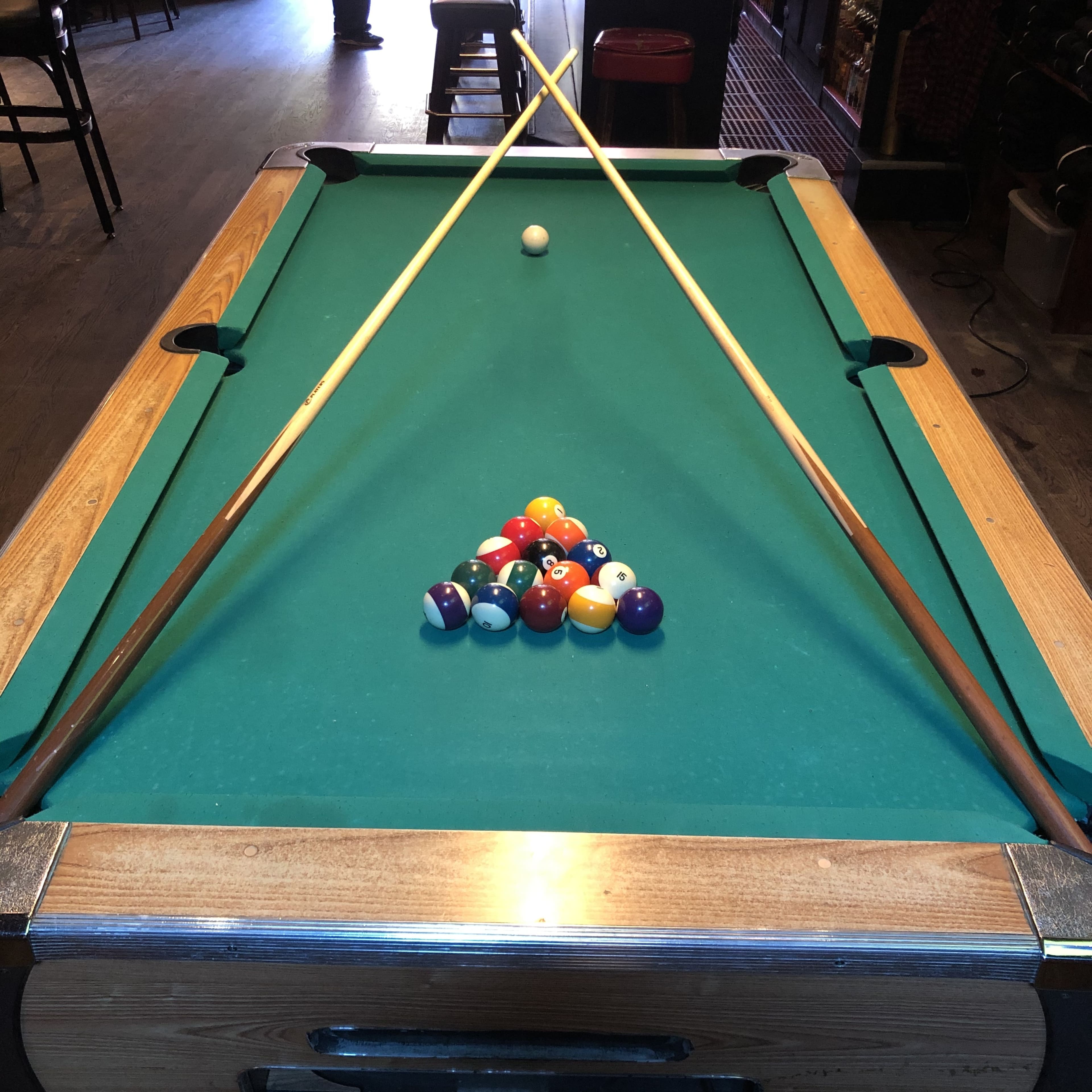 A pool table with a triangle rack of colored balls and two cue sticks resting on the table.