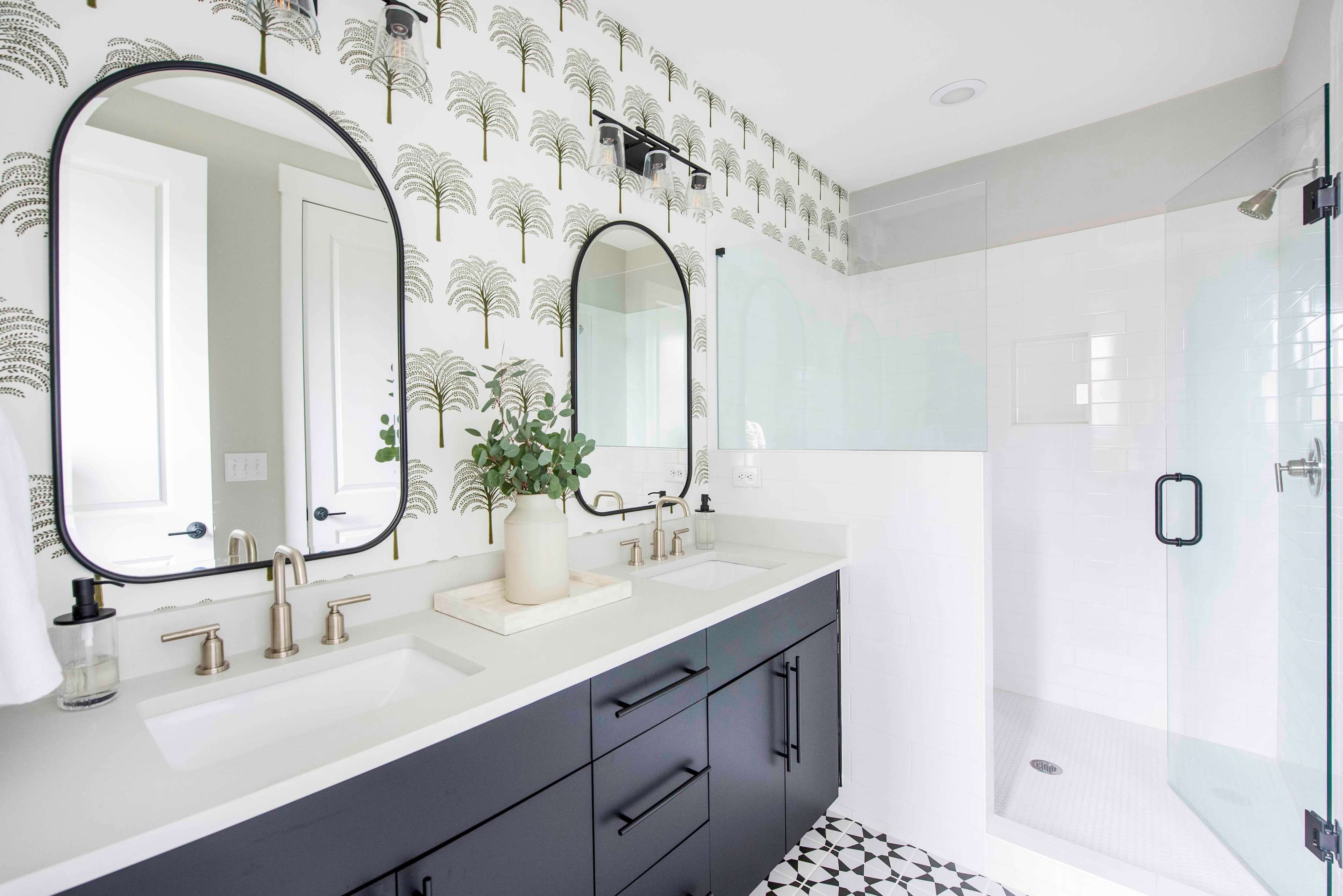 The bathroom features dual sinks with a black cabinet below, framed mirrors, and a shower enclosed by glass, all accentuated by palm tree wallpaper.