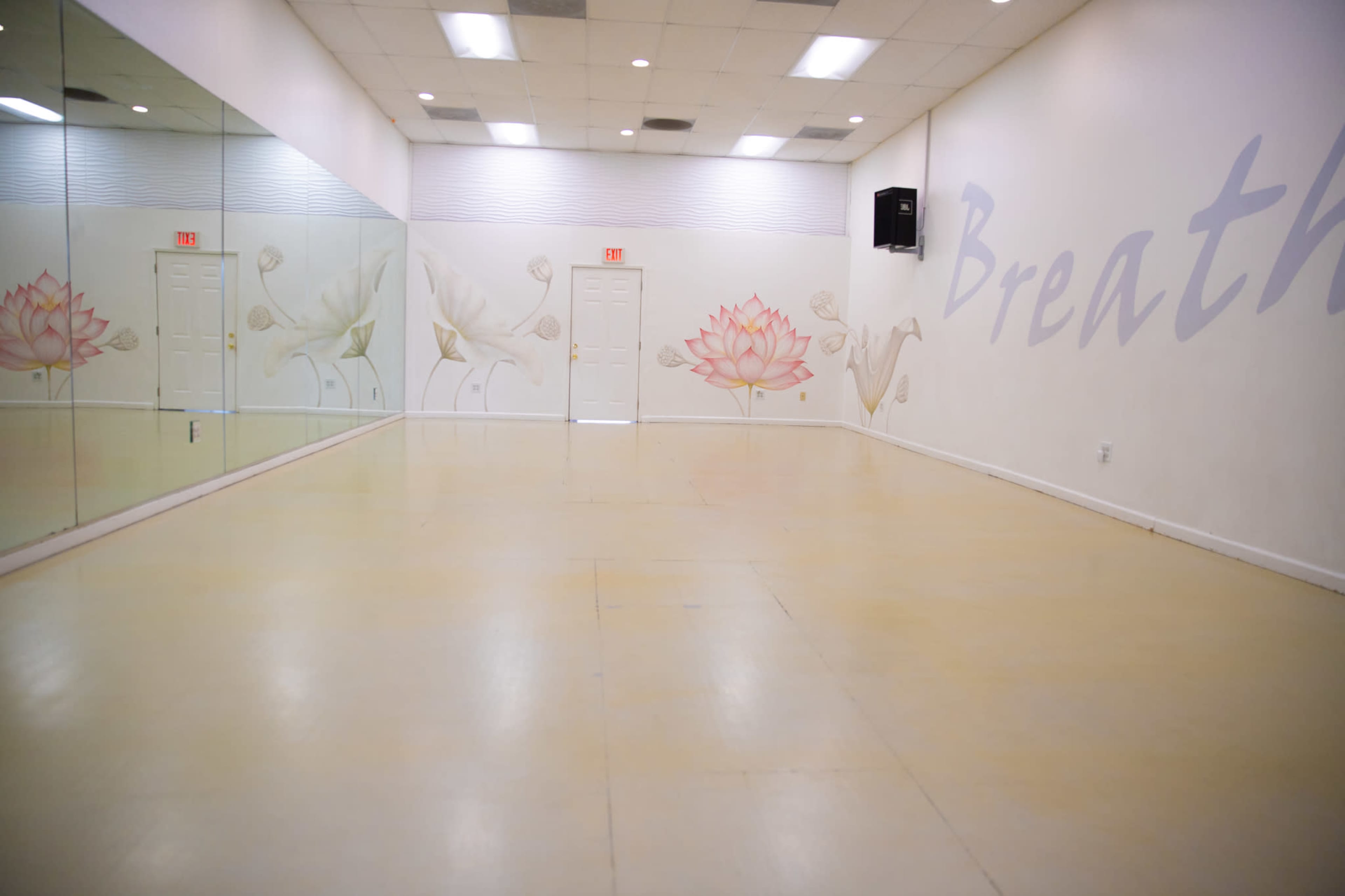 The image shows a blank, spacious room with a mirrored wall and a mural featuring a lotus flower, accompanied by the word "Breathe" painted on the wall.
