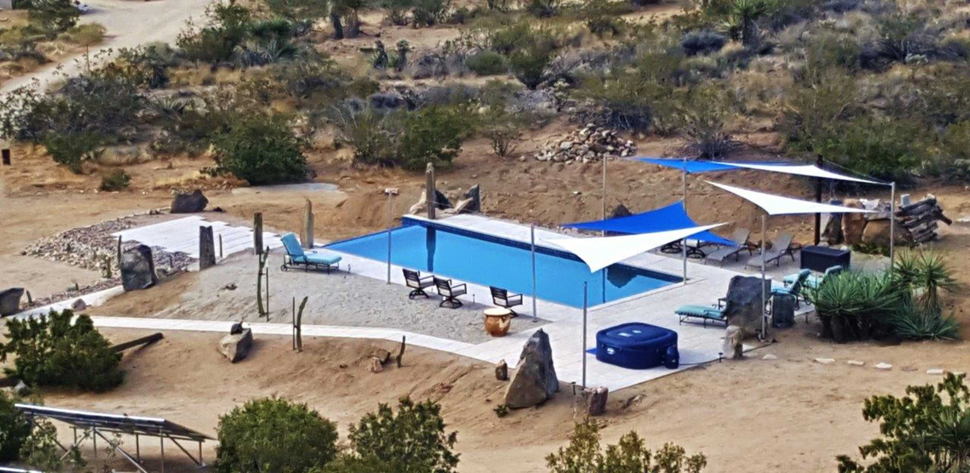 A rectangular swimming pool surrounded by lounge chairs and shaded by white canopies in a desert landscape.