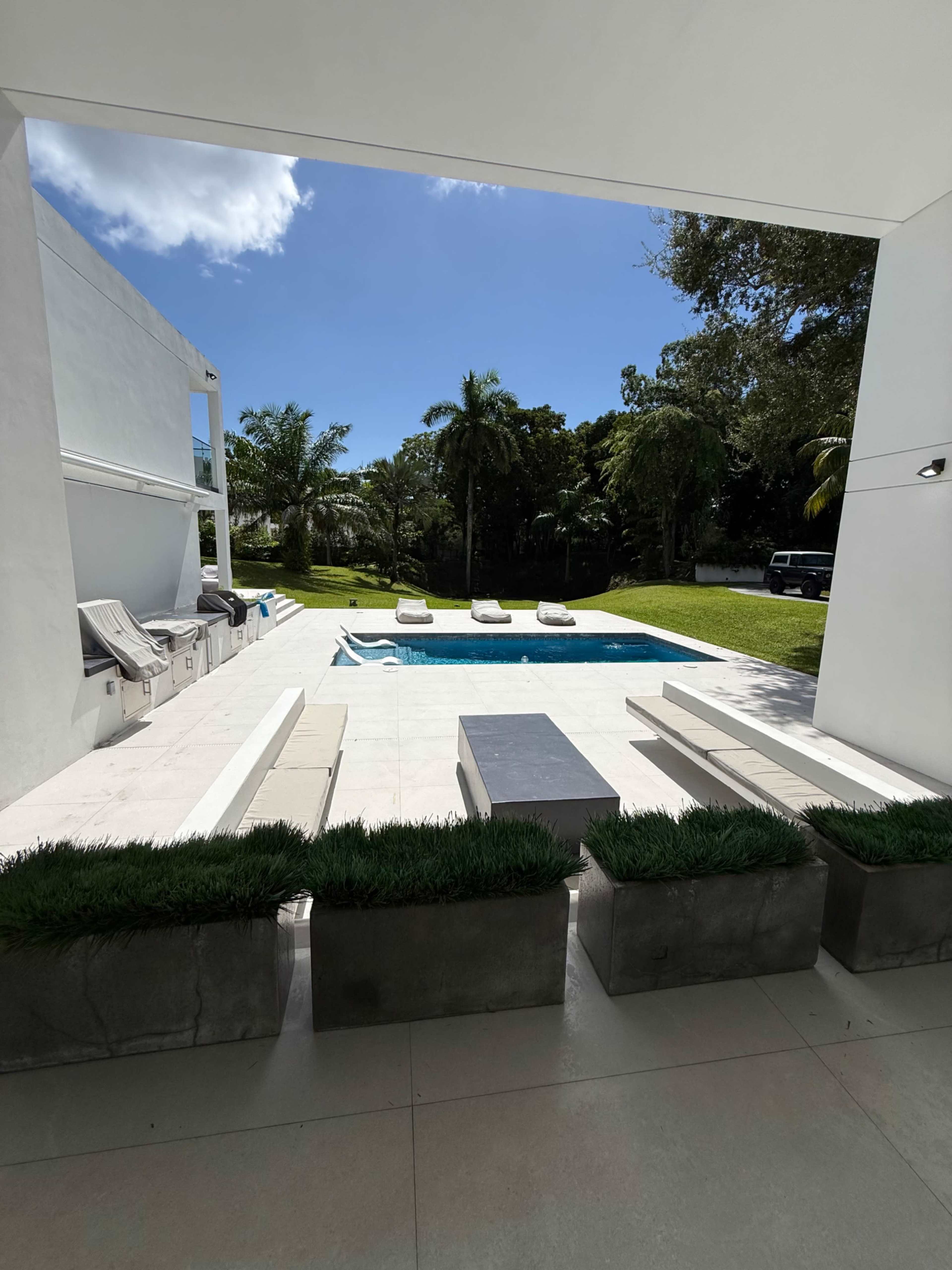 The image shows a modern outdoor area with a swimming pool, lounge chairs, and a grassy landscape.