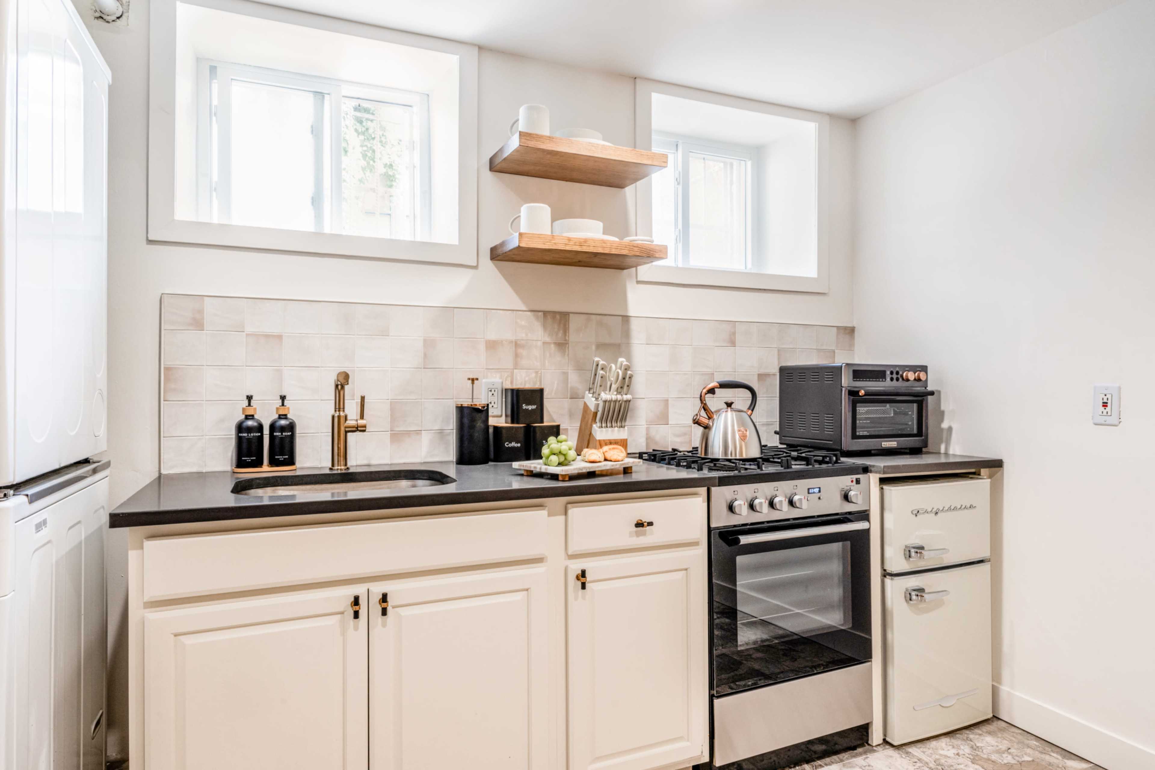 The image shows a modern kitchen featuring white cabinetry, a stainless steel stove, a microwave, and open shelves with dishware.