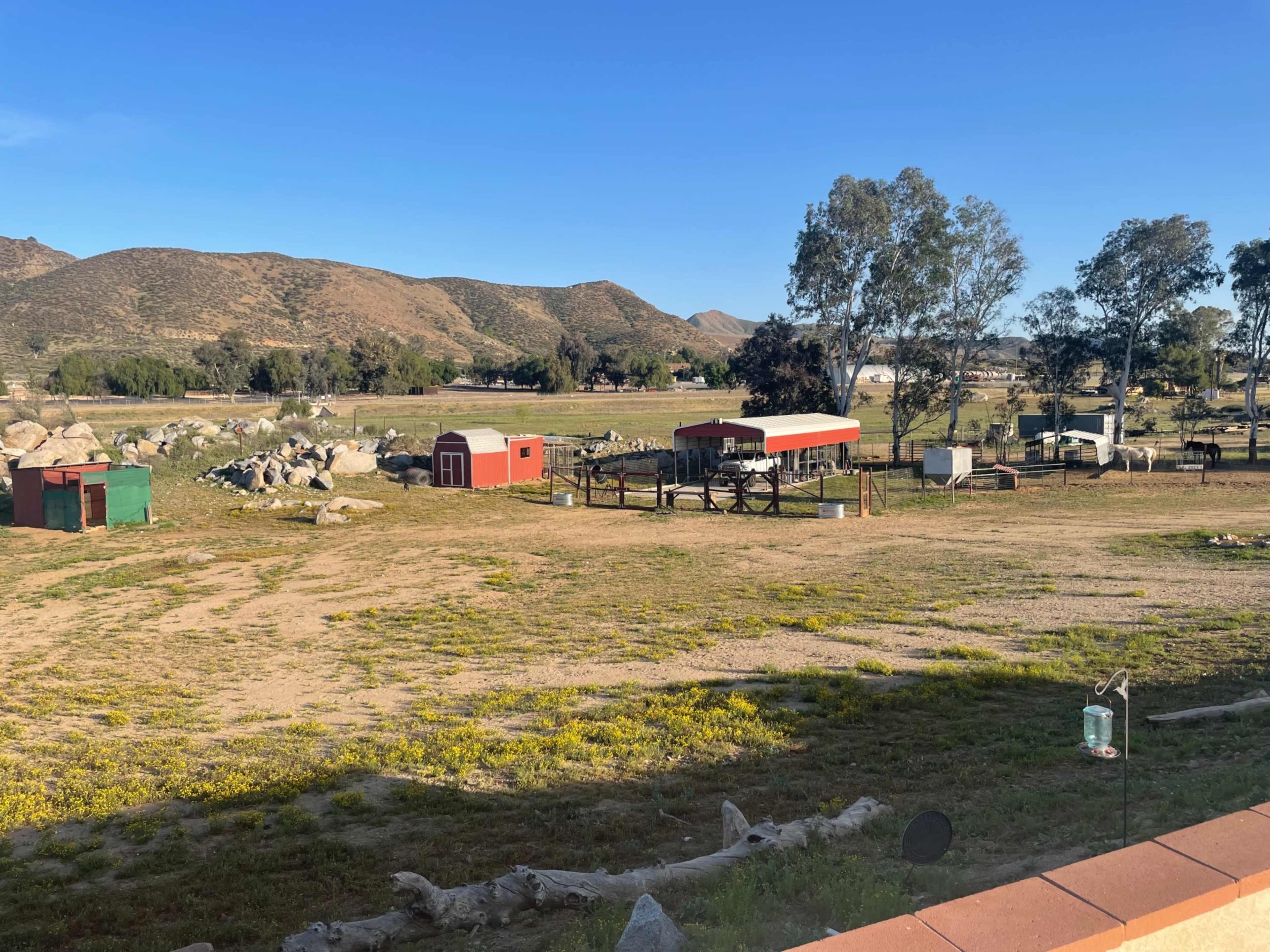 The image shows a rural landscape with several small buildings, a barn, and rocky terrain surrounded by mountains.