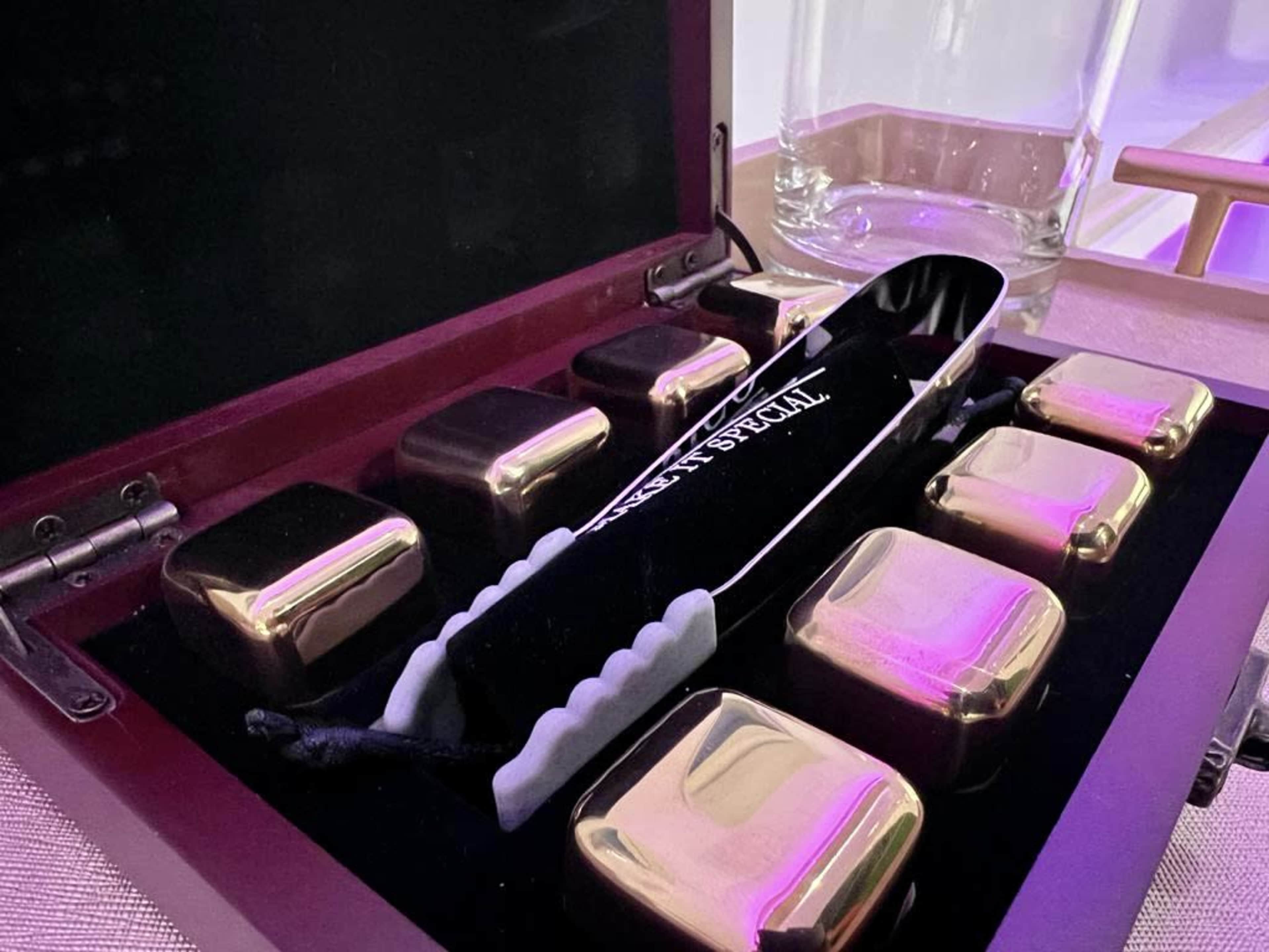 The image shows a velvet-lined box containing a set of seven gold-colored cubes and a pair of tongs.