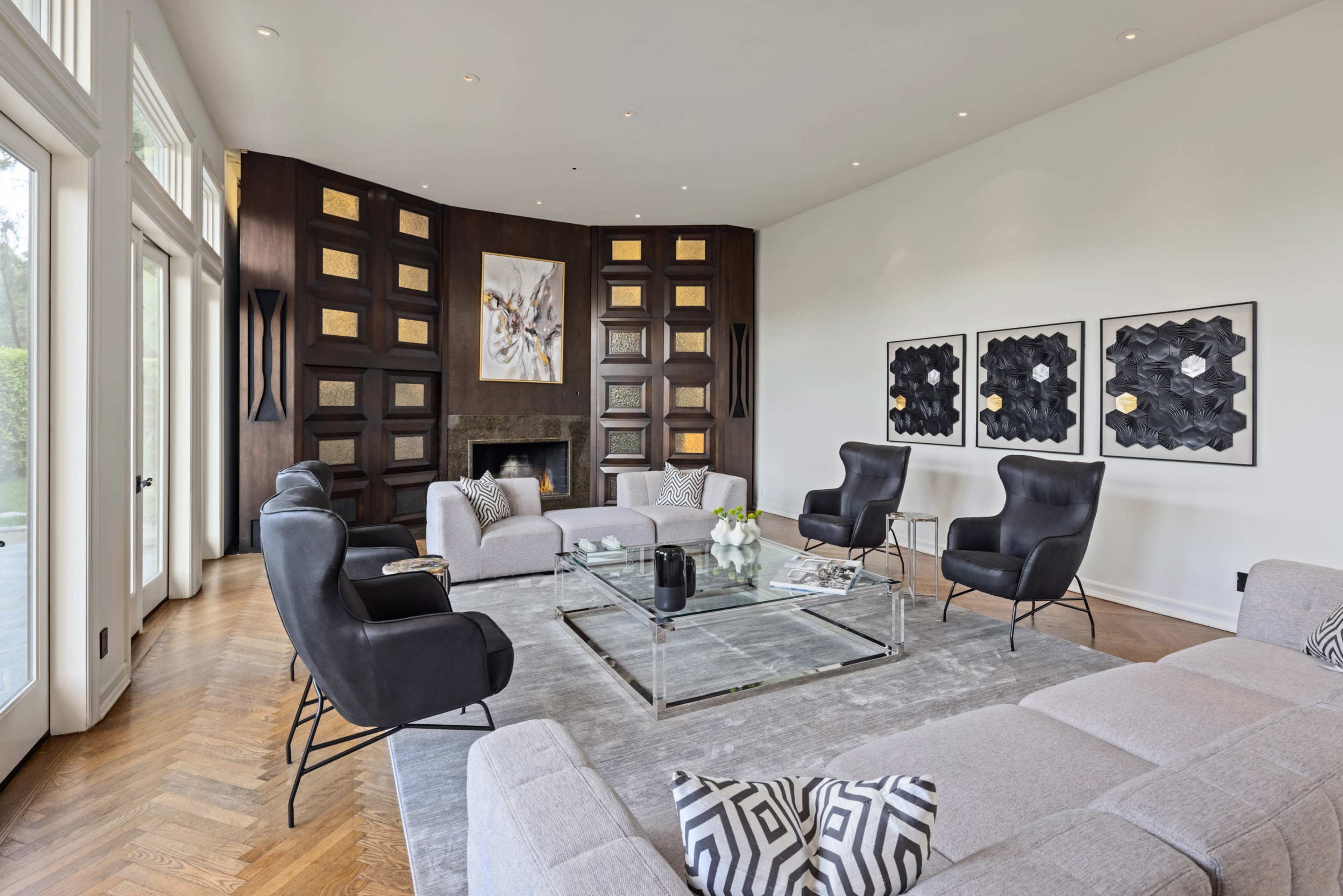 A modern living room featuring a curved wall with geometric artwork, a glass coffee table, and a mix of black and gray seating options.