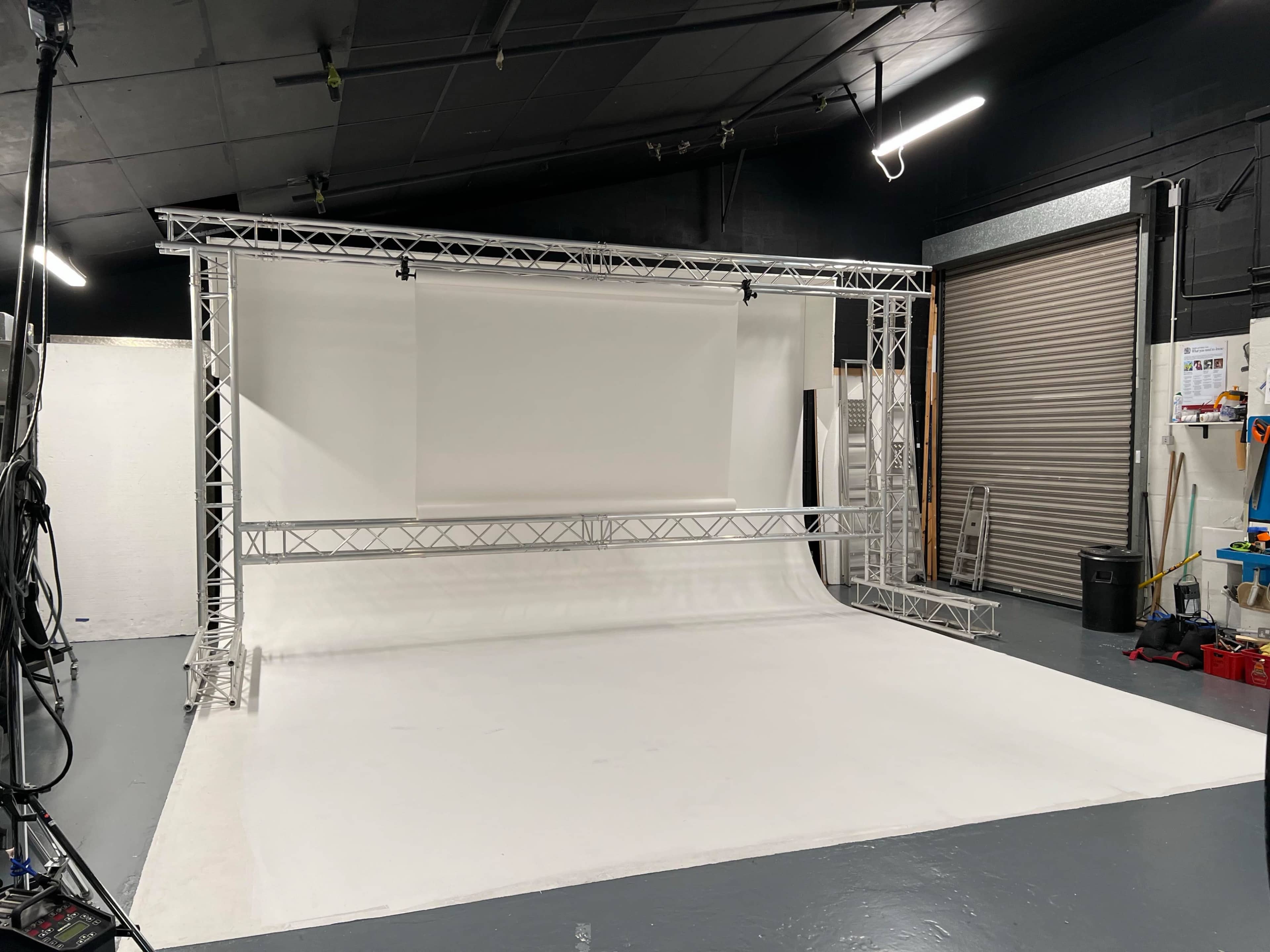 A photography studio with a white backdrop, supported by a metal truss frame, and various equipment scattered around.