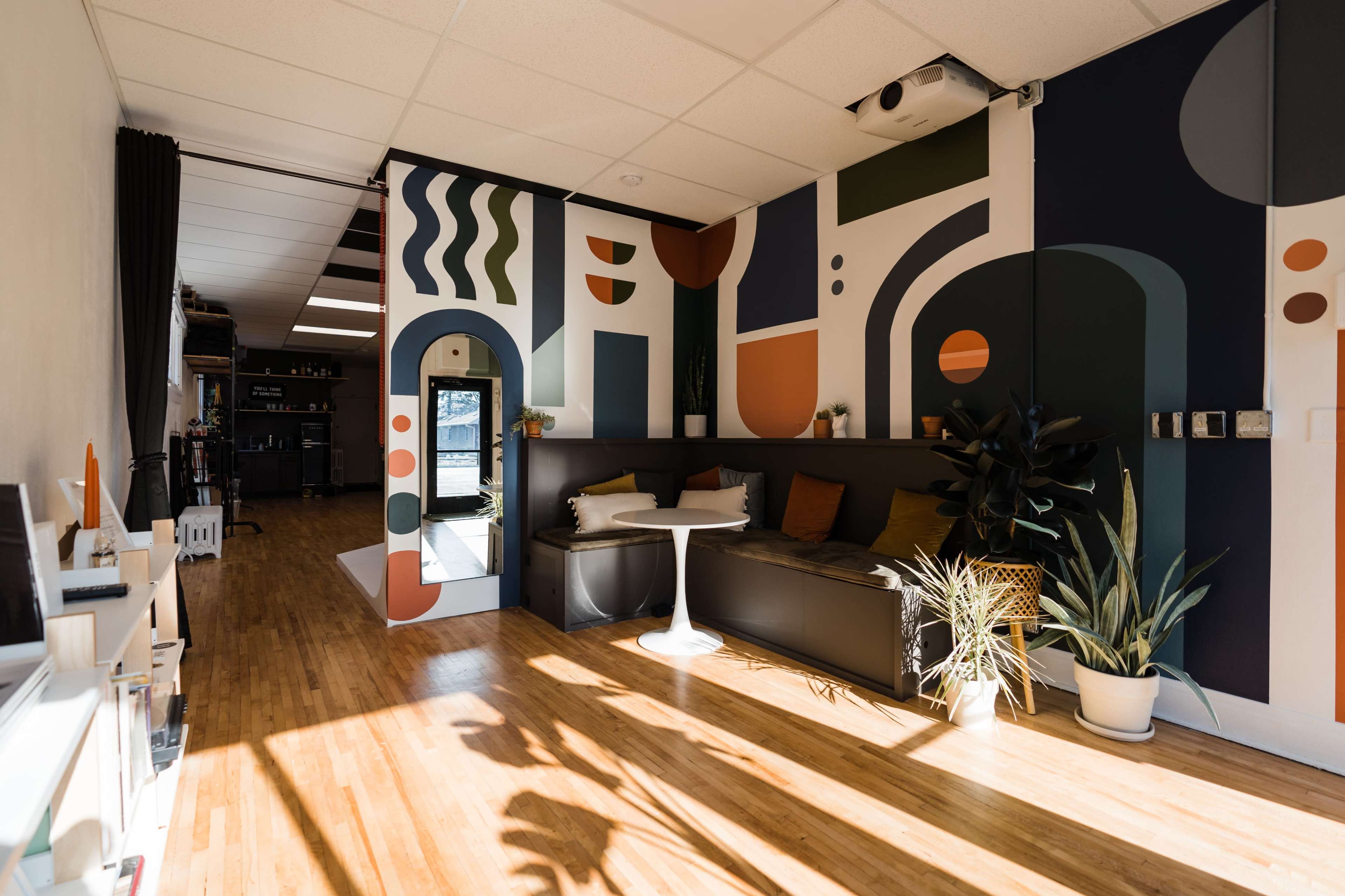 A brightly lit room featuring a modern design with colorful abstract wall art, a black couch, and potted plants.
